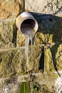 Icicles hang from a pipe on a stone wall