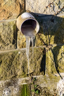 Icicles hanging from a pipe on a stone wall