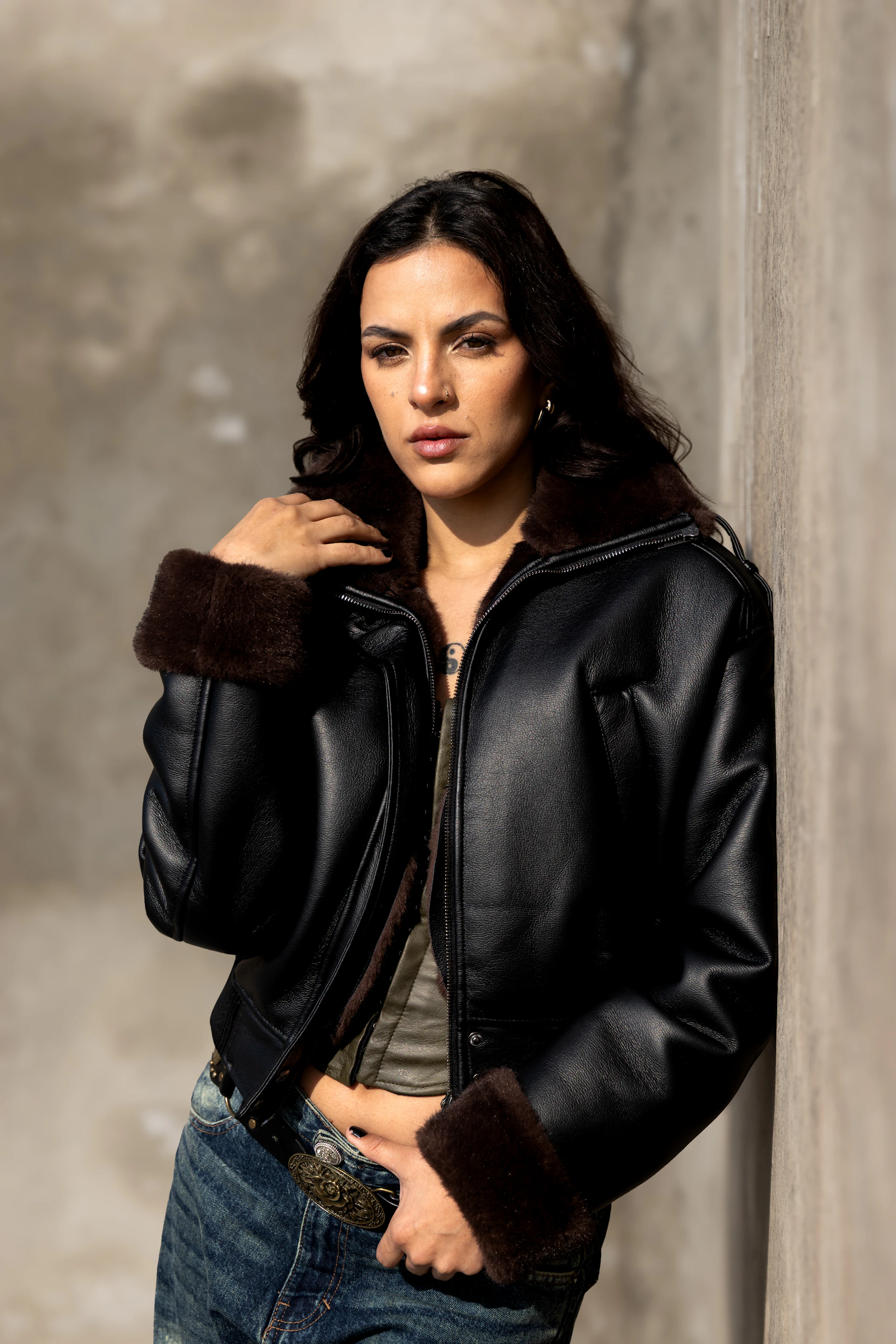 A woman in a leather jacket leans against a wall.