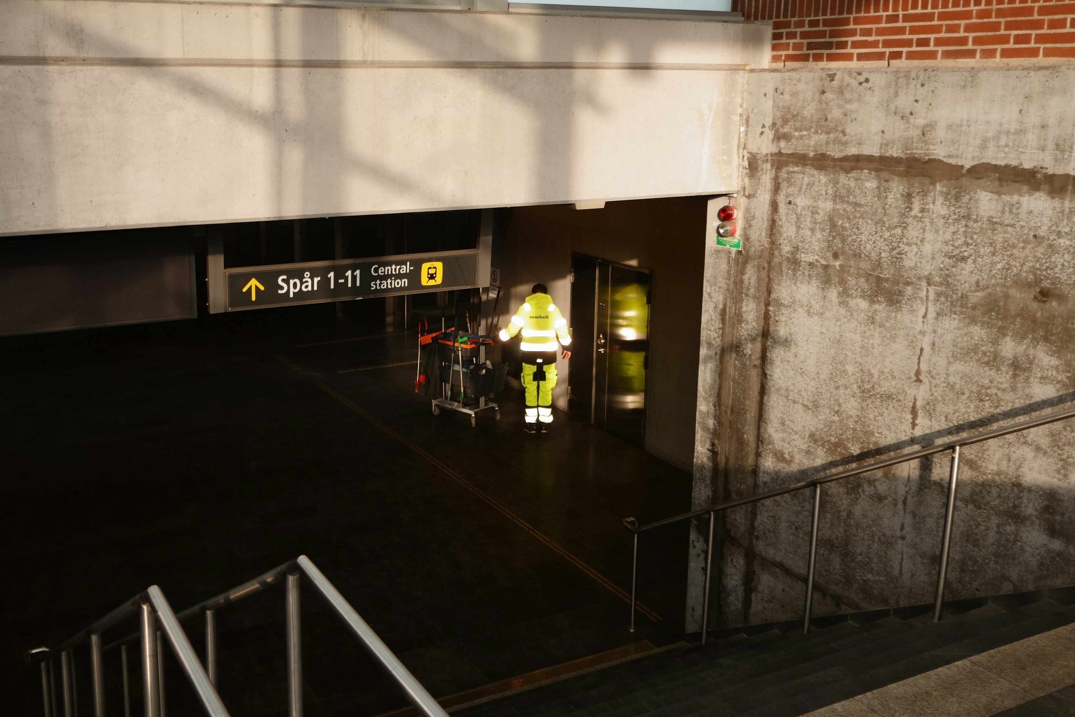 Worker in reflective vest pushes luggage cart in subway station.
