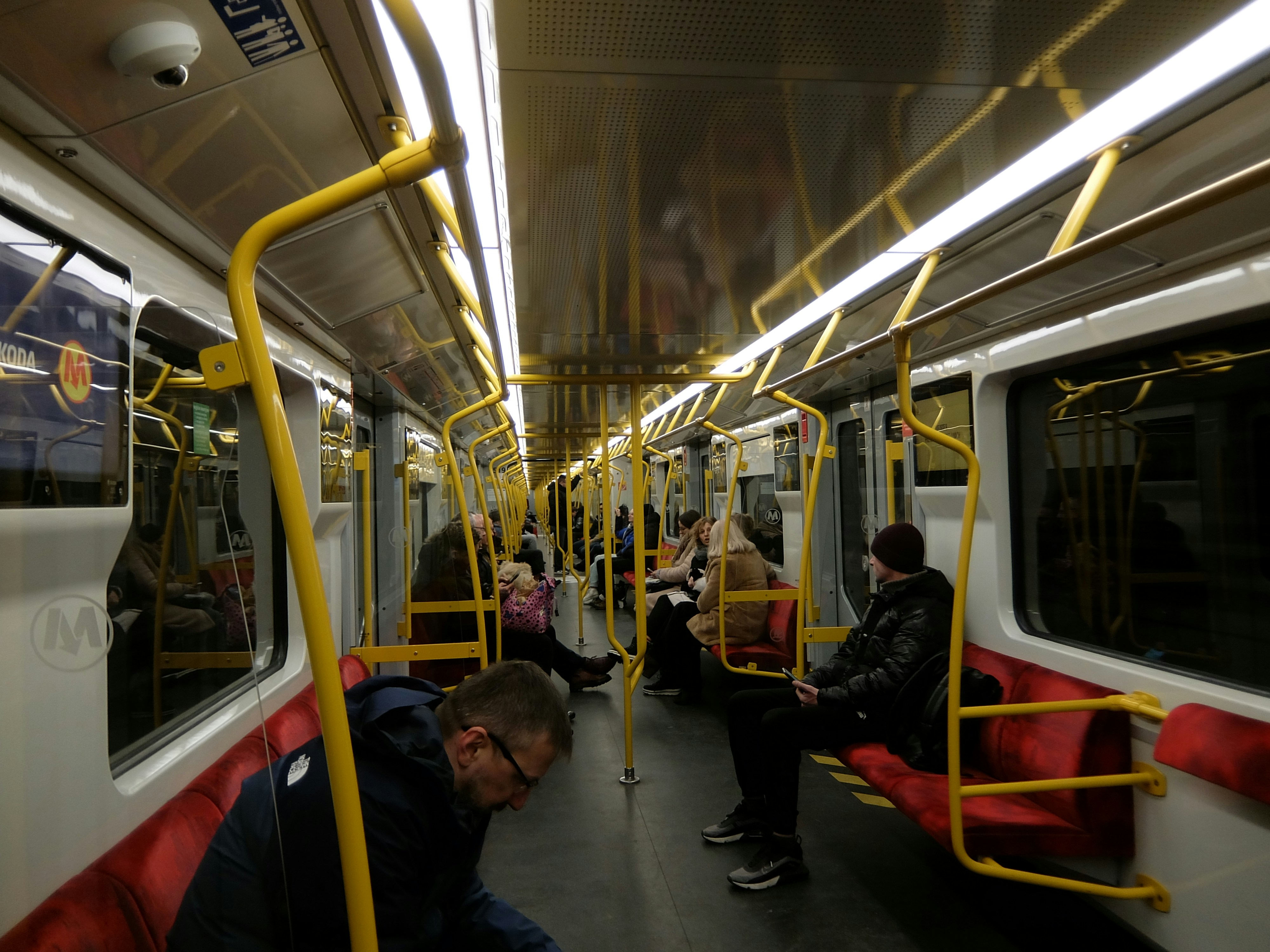 People sitting inside a subway train with yellow poles.