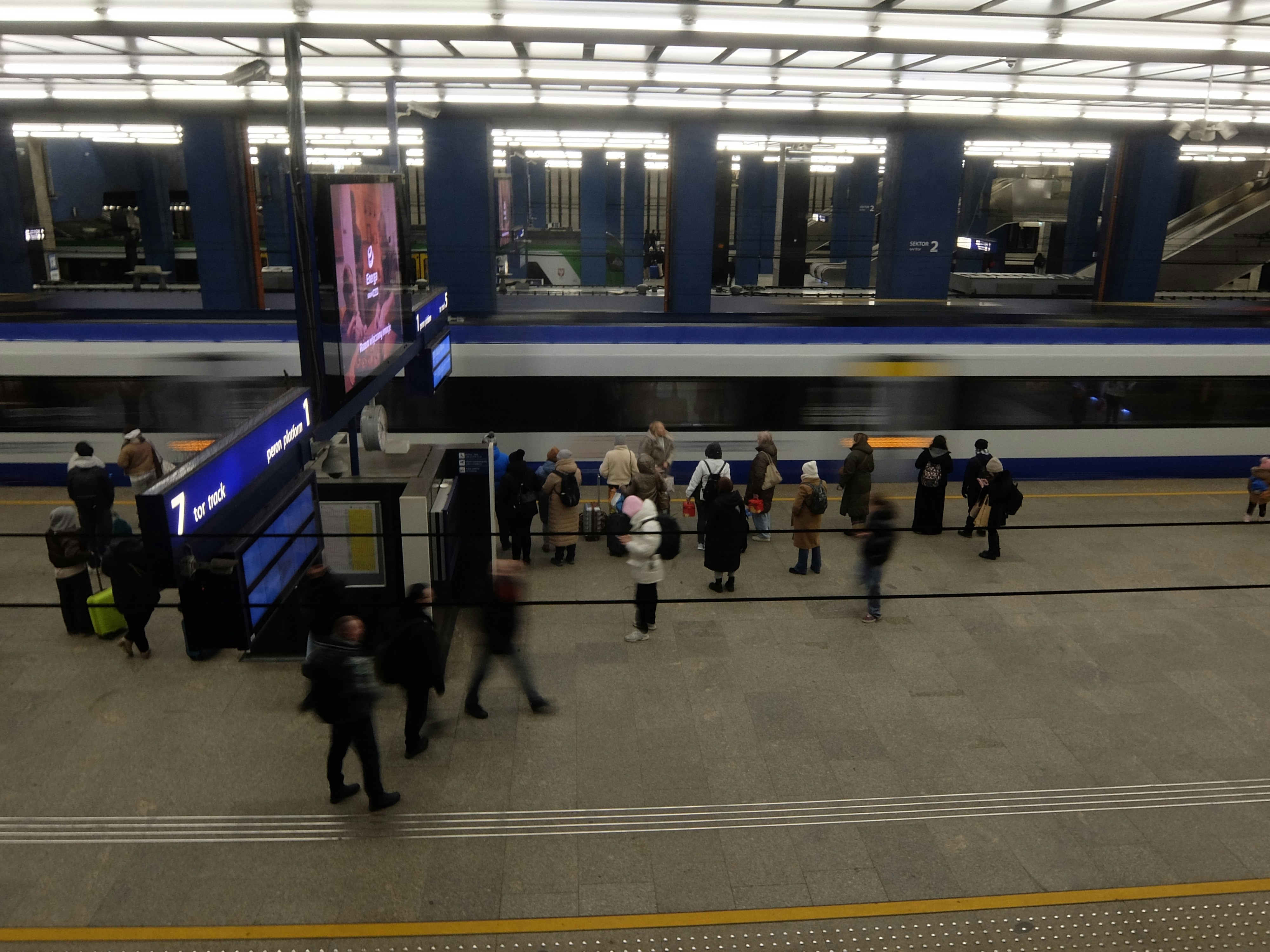 People waiting on a train platform as a train passes.