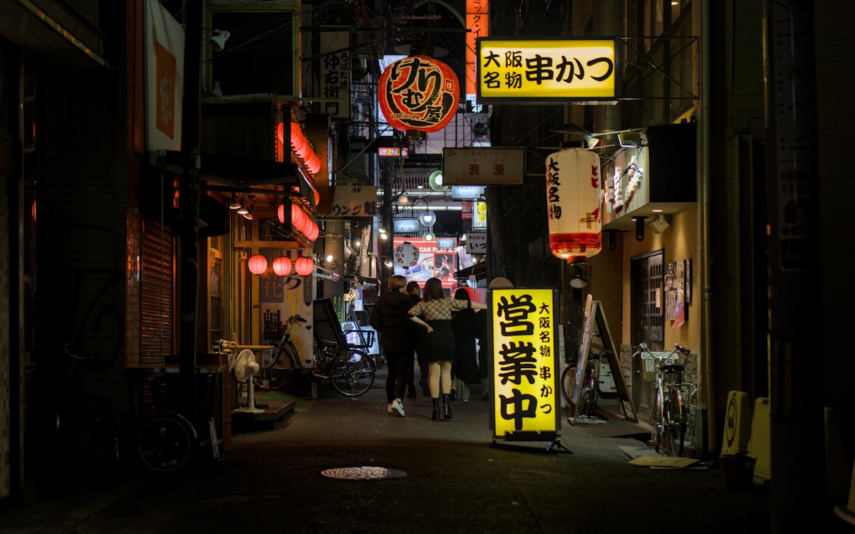 Ruelle étroite d'Osaka la nuit, illuminée par des enseignes néon et des lanternes de restaurant japonais