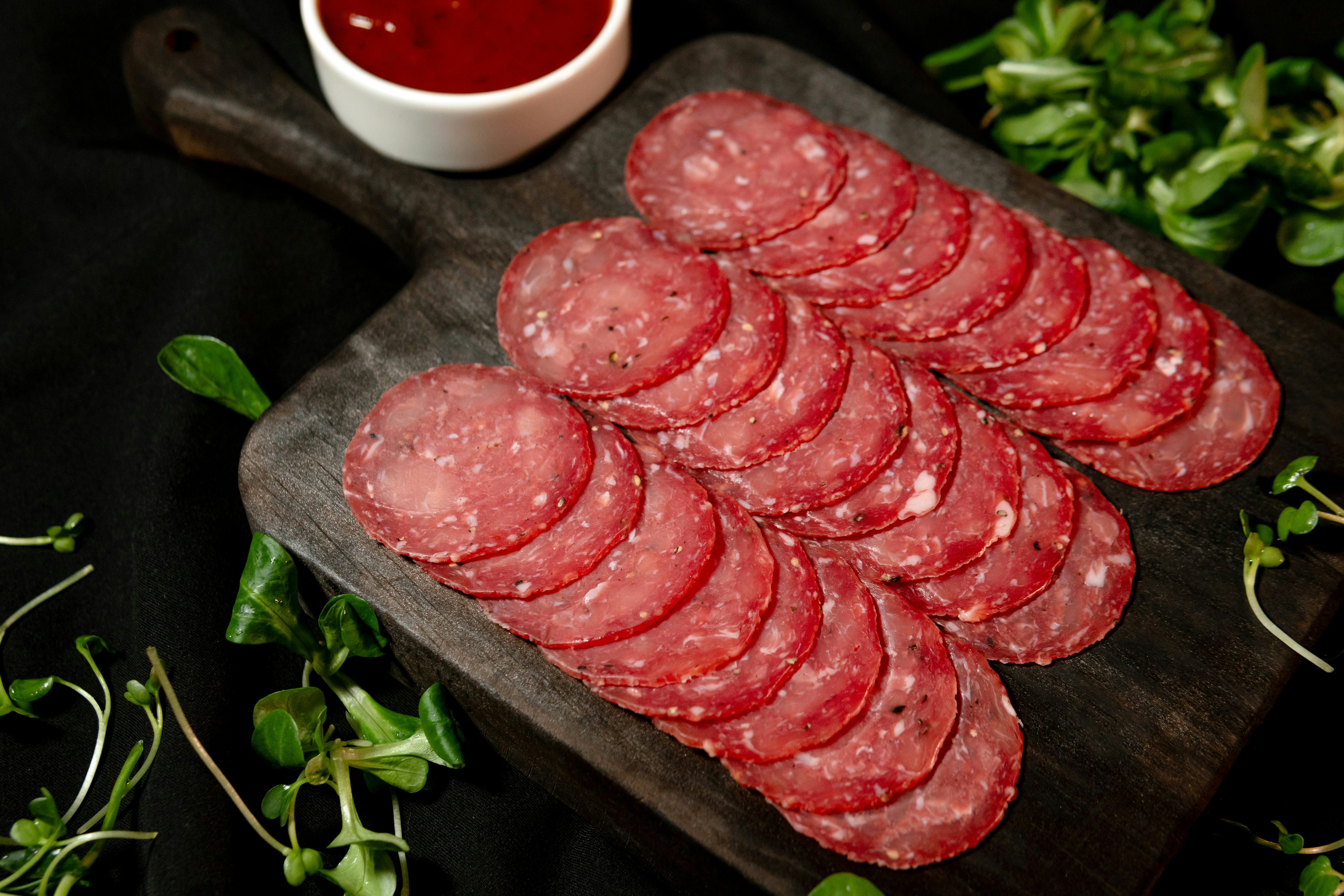 Thinly sliced salami on a wooden board with sauce.