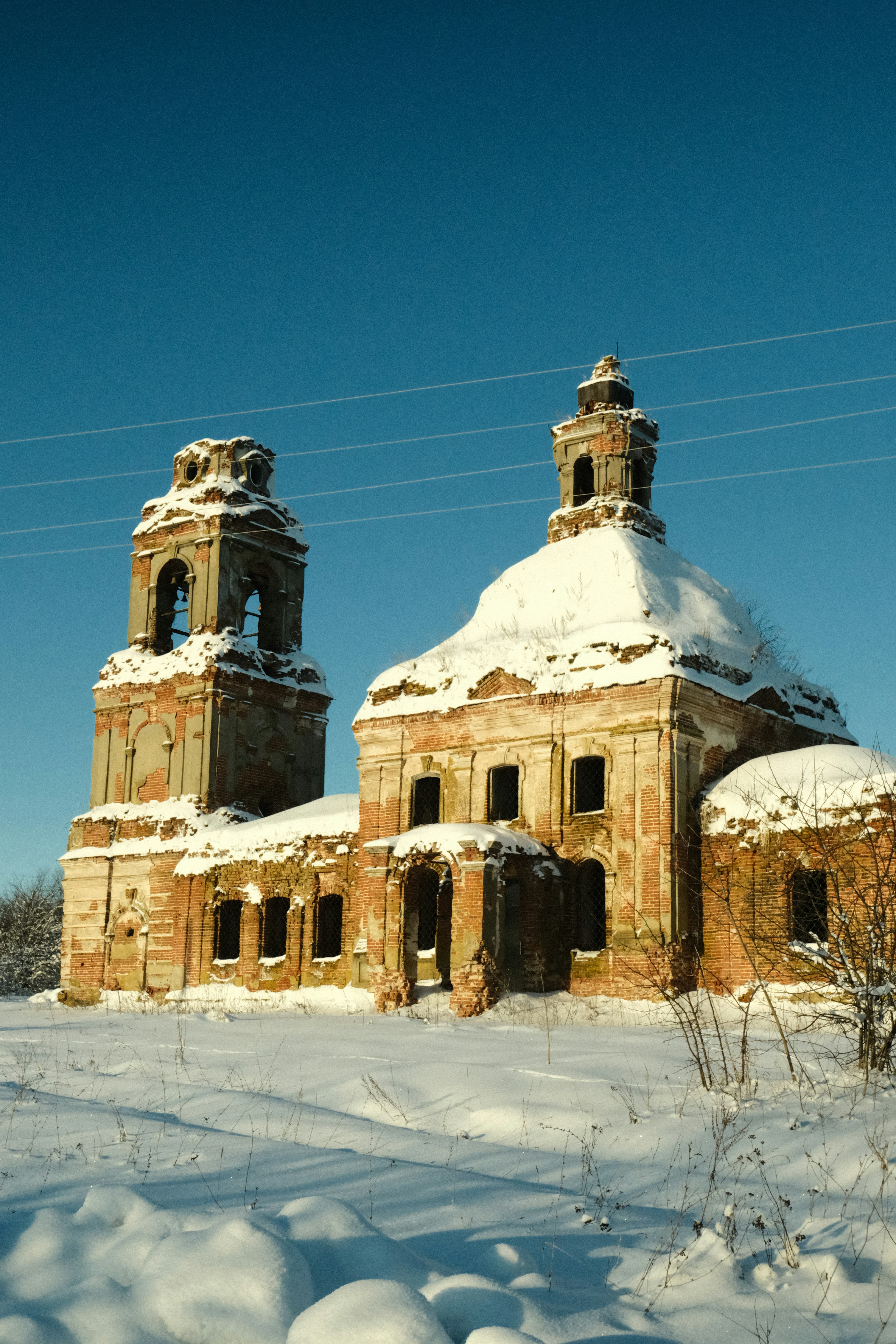 Abandoned brick church covered in snow under a clear sky
