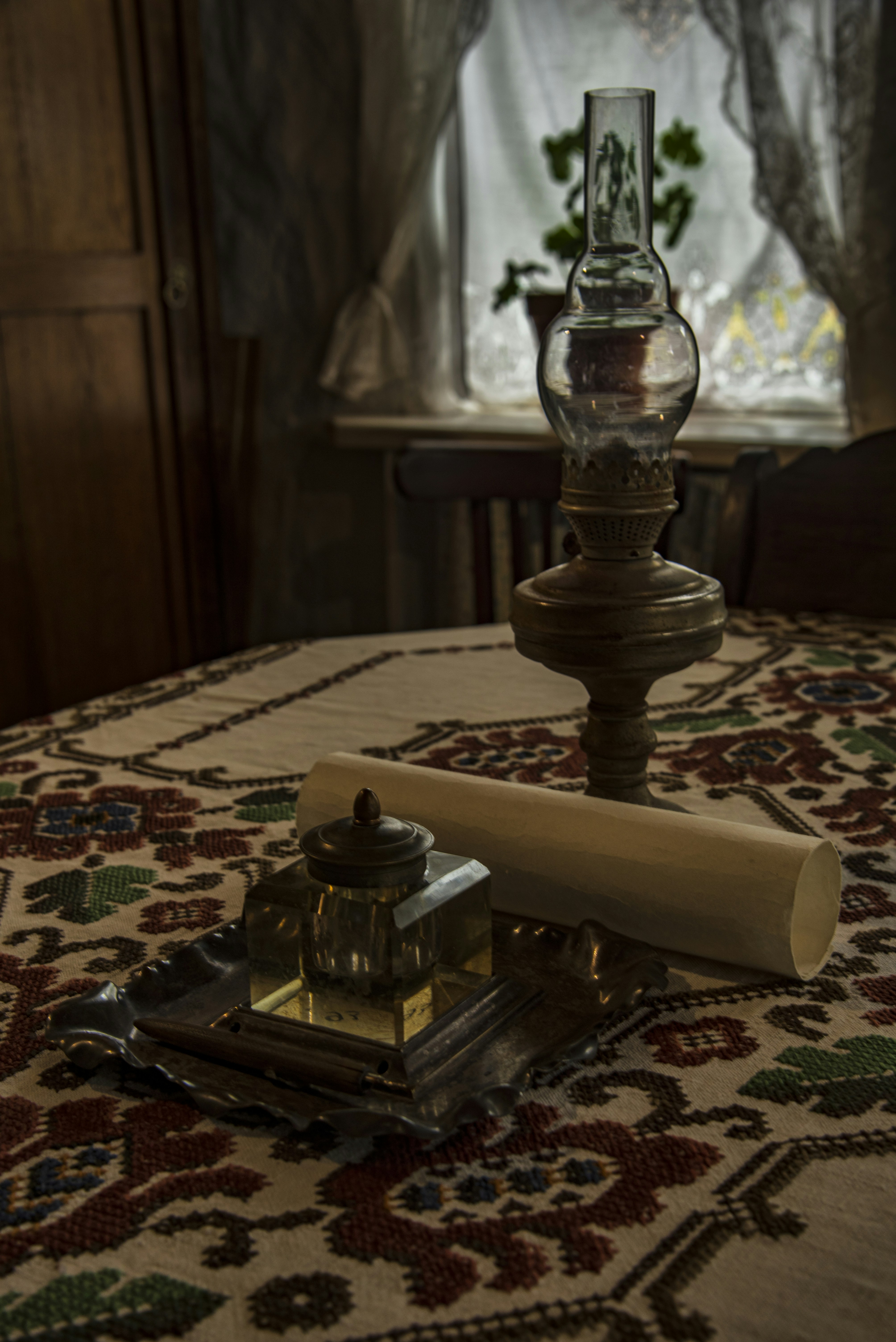 Antique oil lamp and inkwell on a patterned tablecloth.