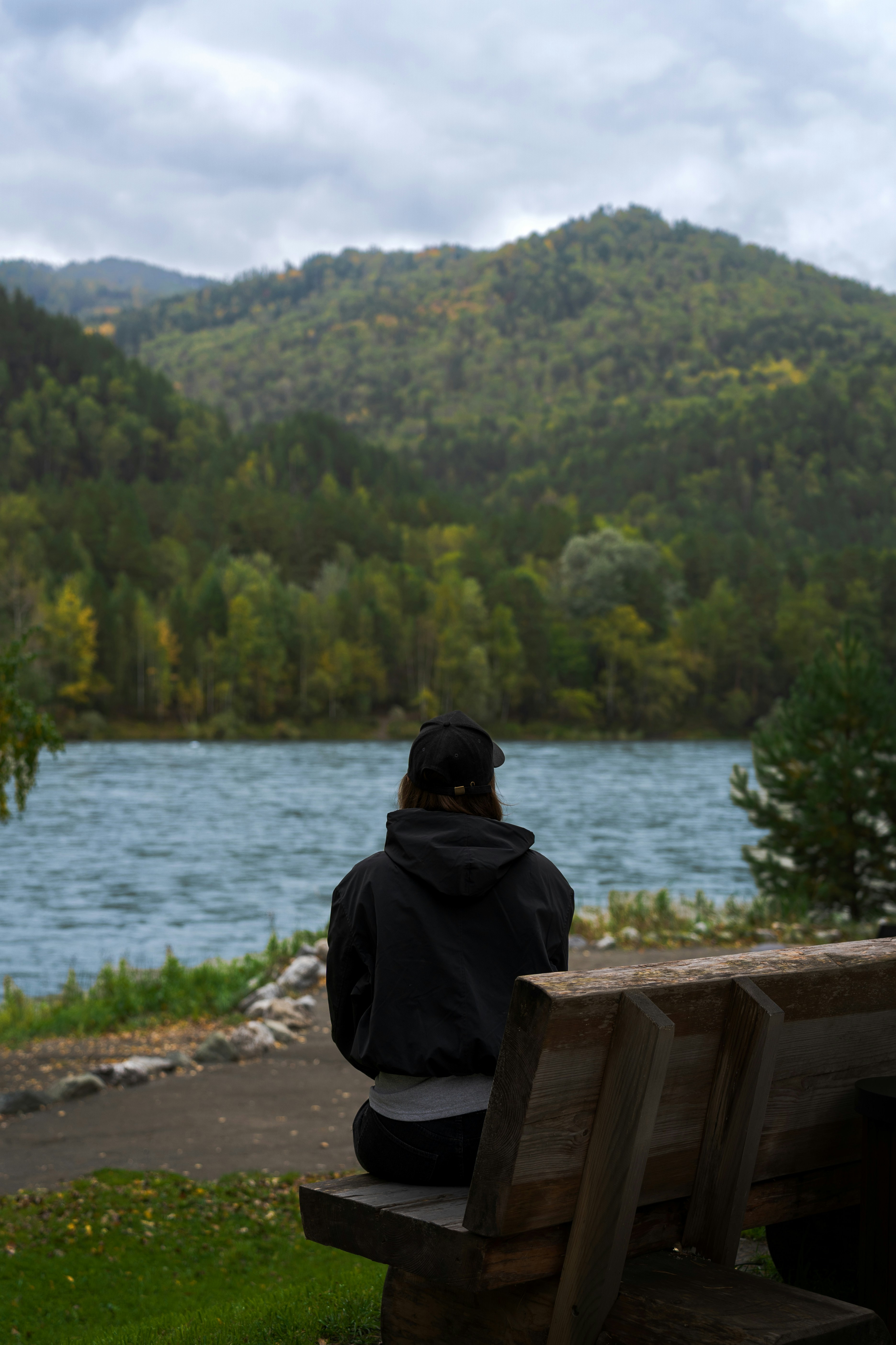Person sitting on bench overlooking lake and mountains.