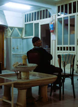 Elderly man sitting in a dimly lit room.