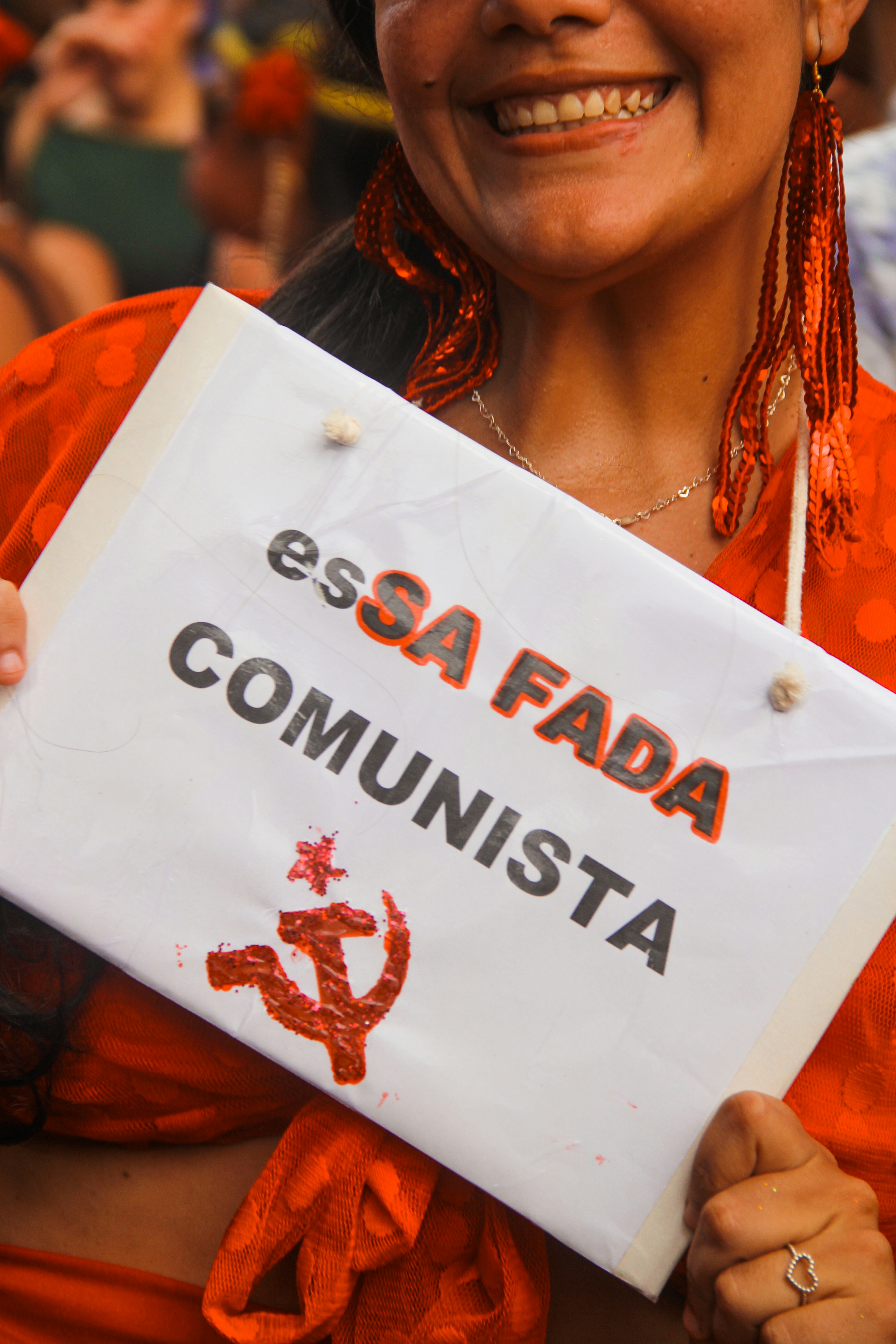 Woman holds sign with communist symbol and portuguese text.