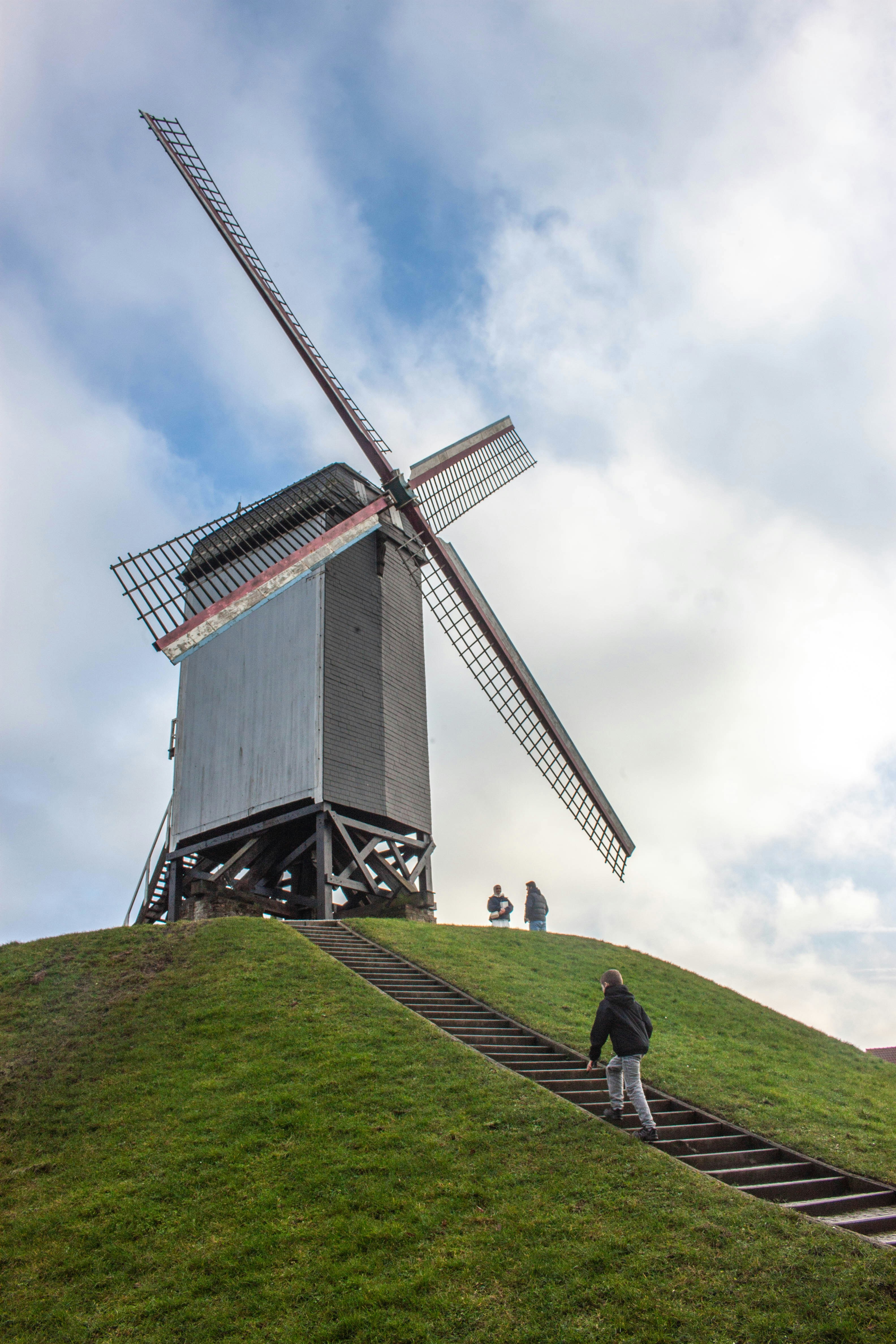 Wooden windmill on a grassy hill with stairs.