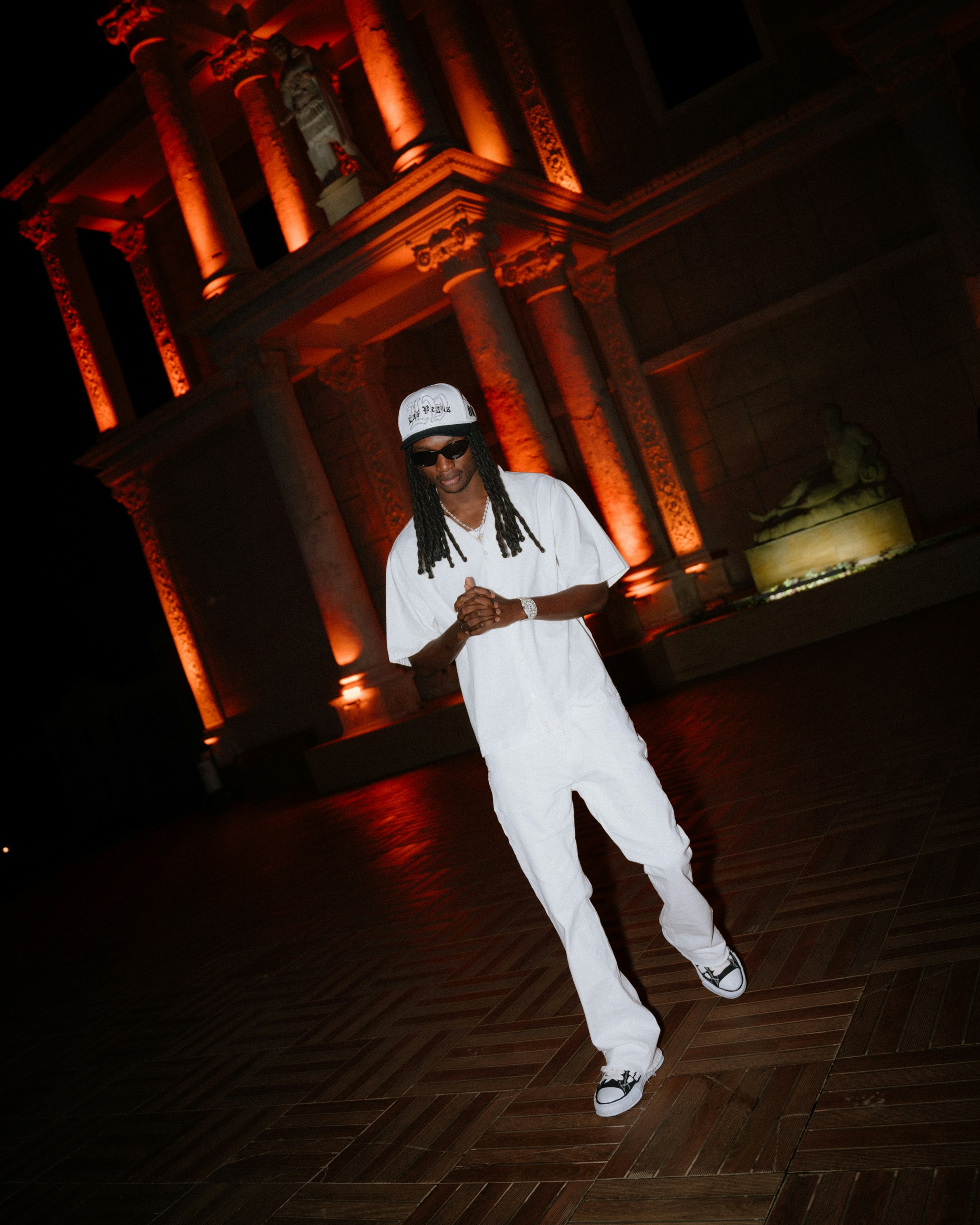 白い服を着た男が明かりのついた建物の外に立っている