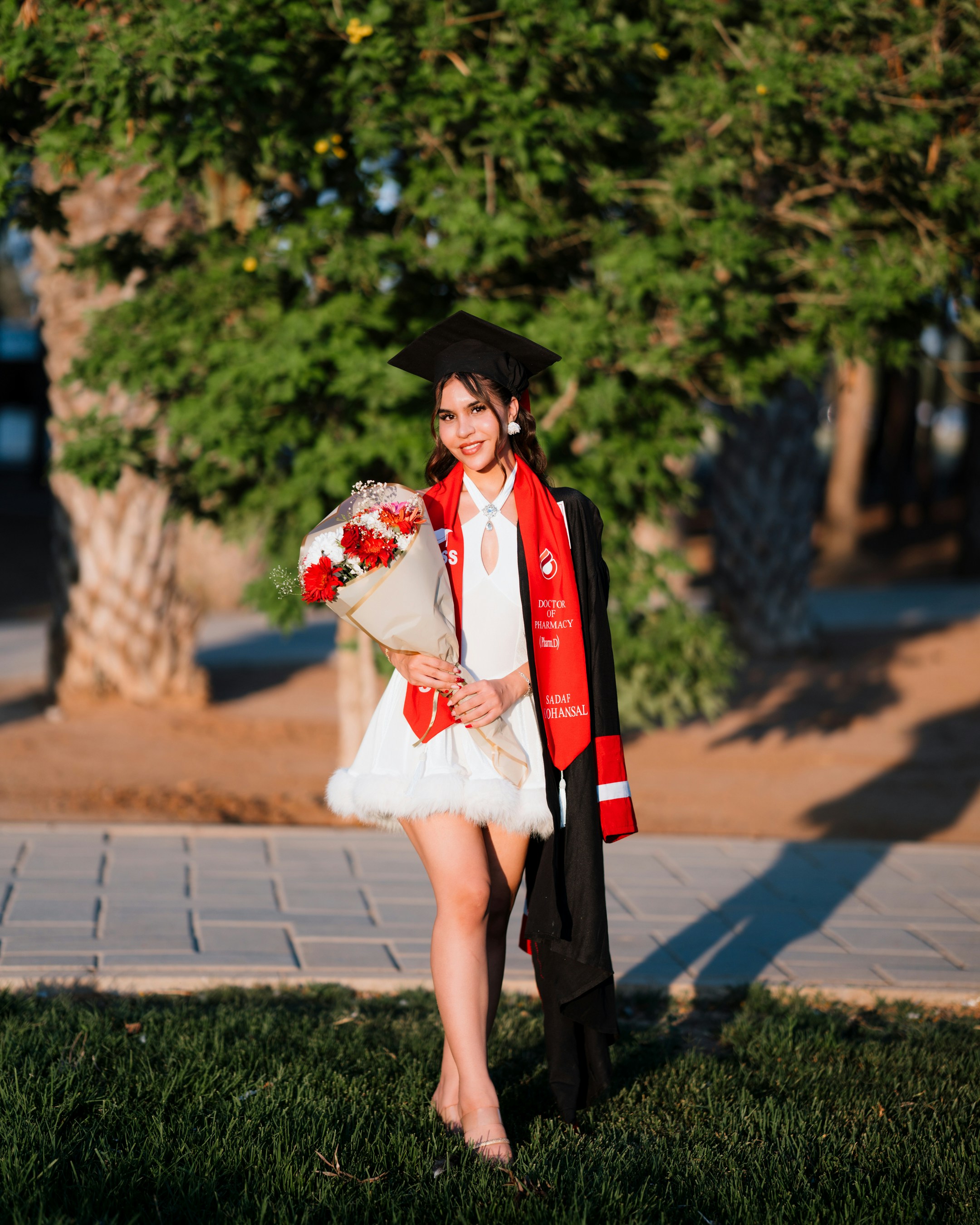 A smiling graduate in a cap and gown holding flowers photo – Free ...