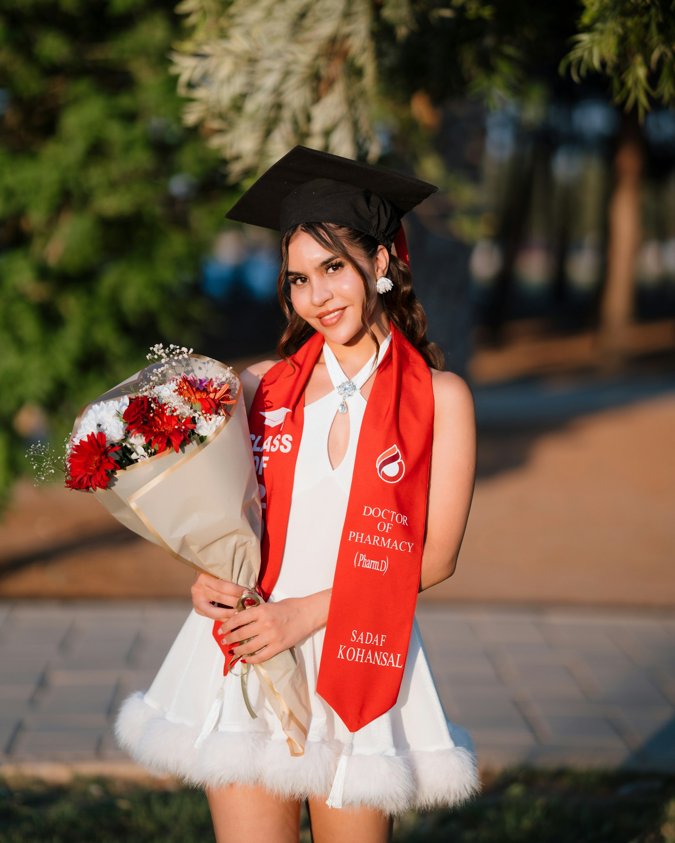 A smiling graduate holds a bouquet of flowers.