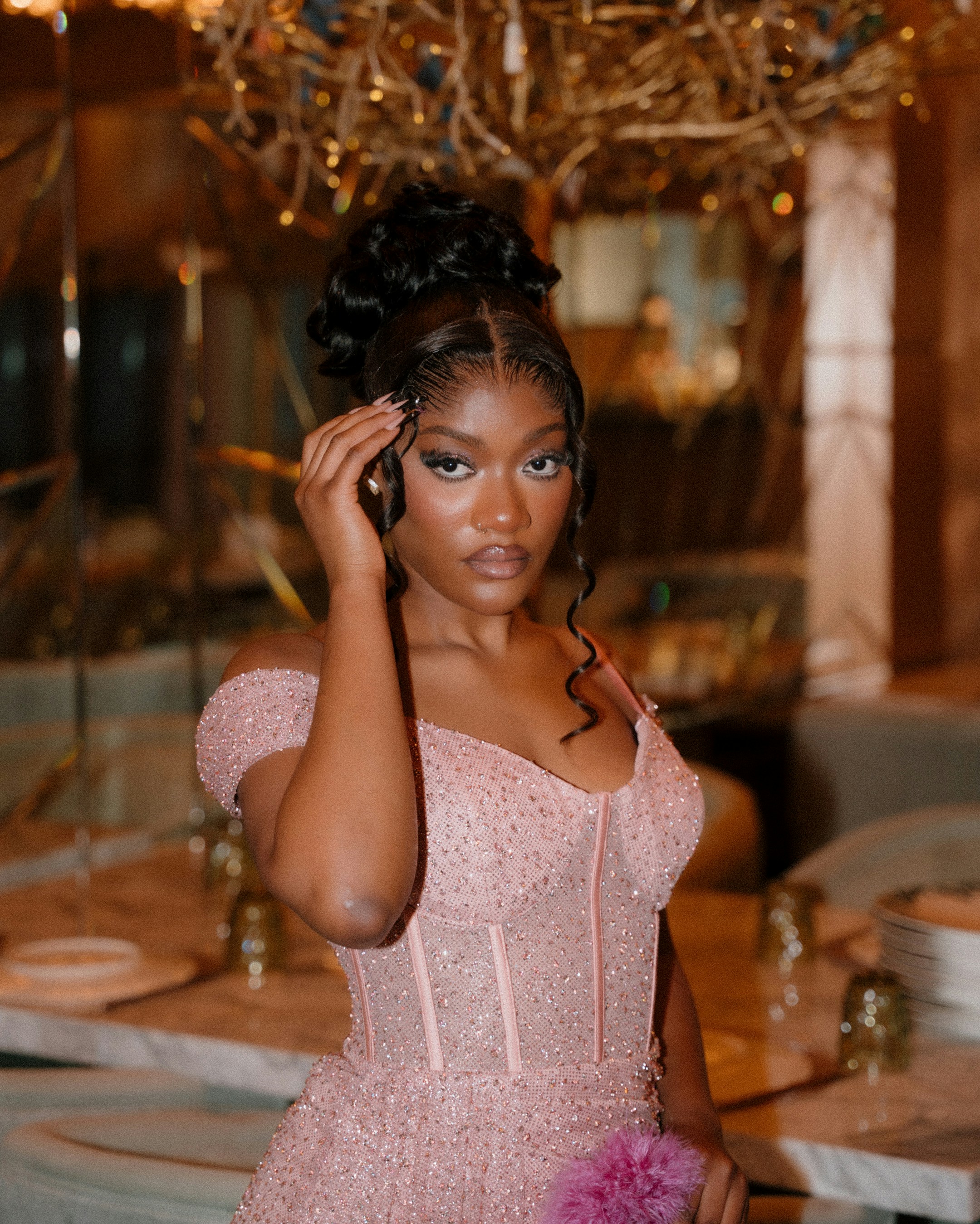 Young woman in a sparkly pink dress poses elegantly.