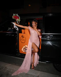 Woman in pink dress holding flowers exiting a car