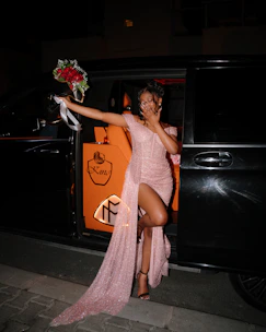 Woman in pink dress holding flowers exiting a car