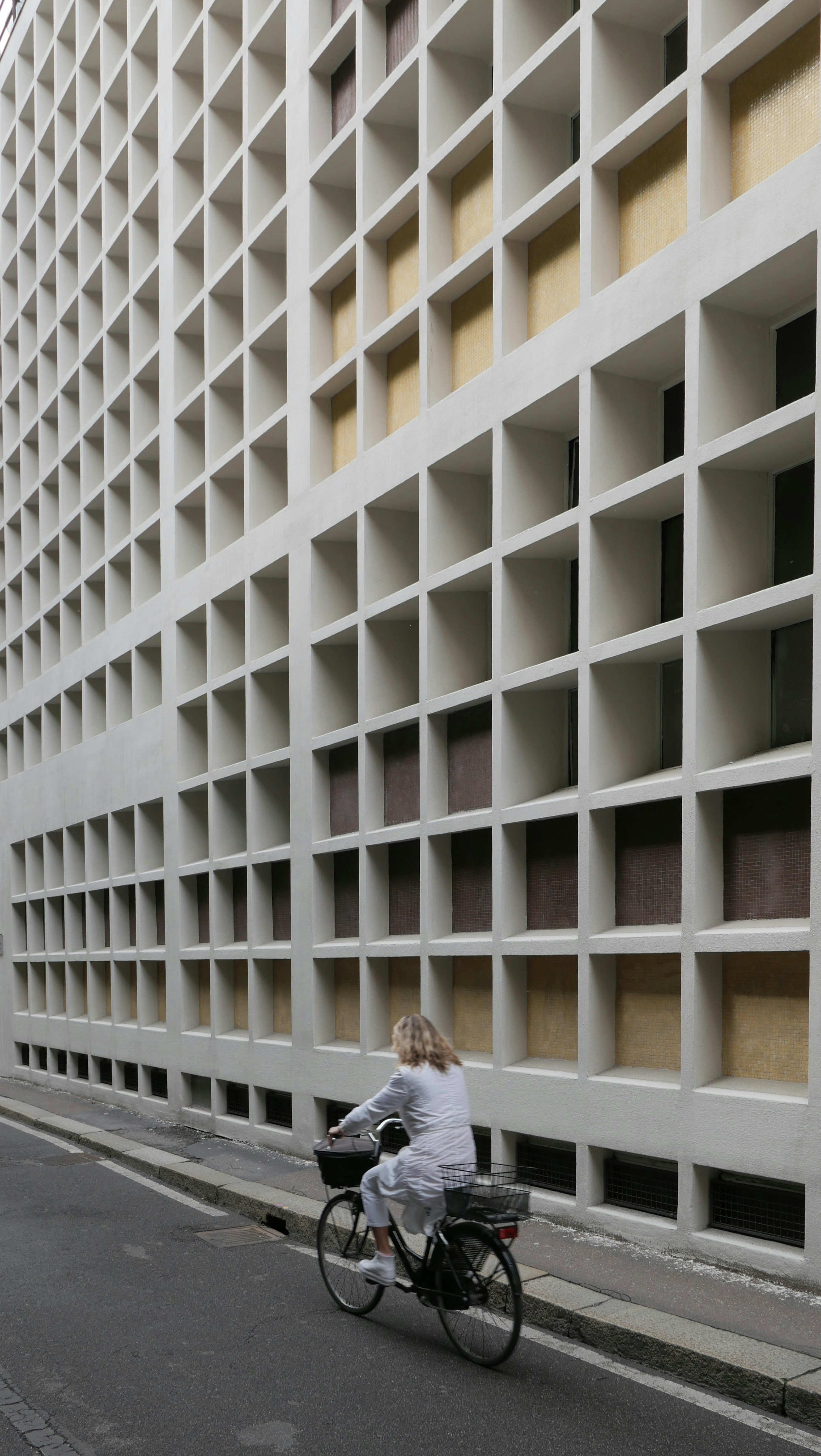Una donna passa in bicicletta davanti a un edificio con una facciata a griglia