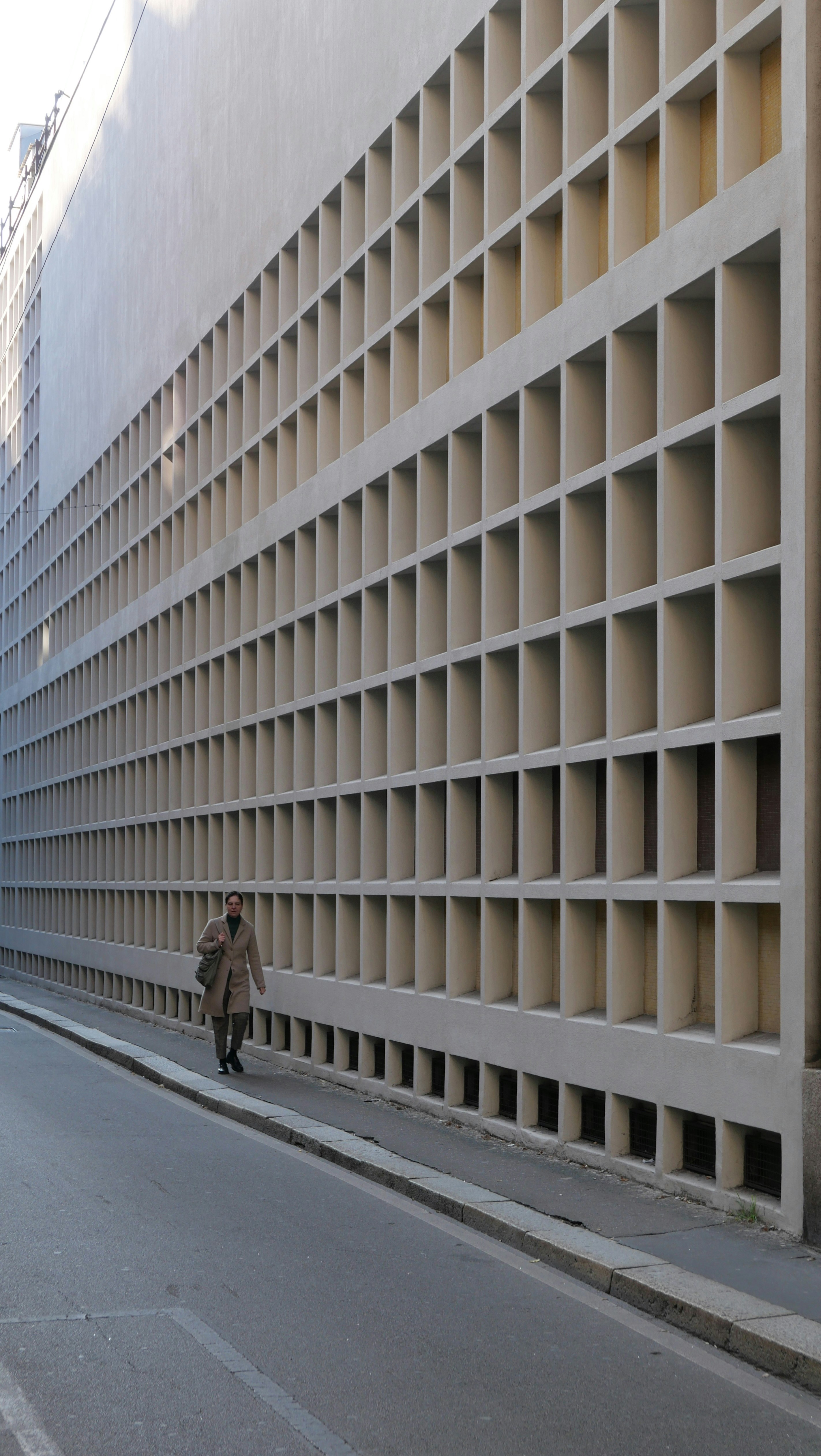 Una persona passa davanti a un edificio con una facciata a griglia.
