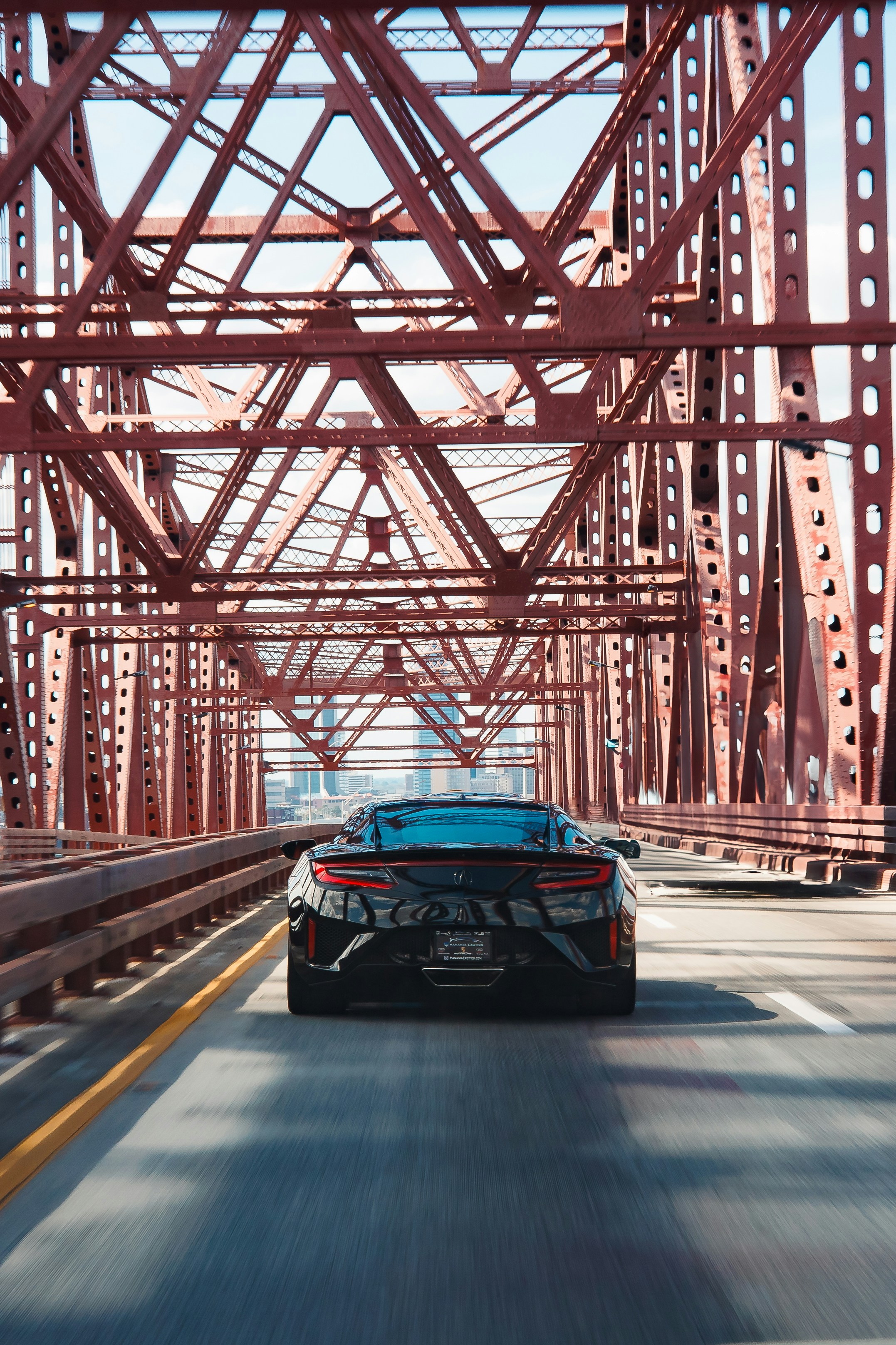 Black sports car driving on a red metal bridge