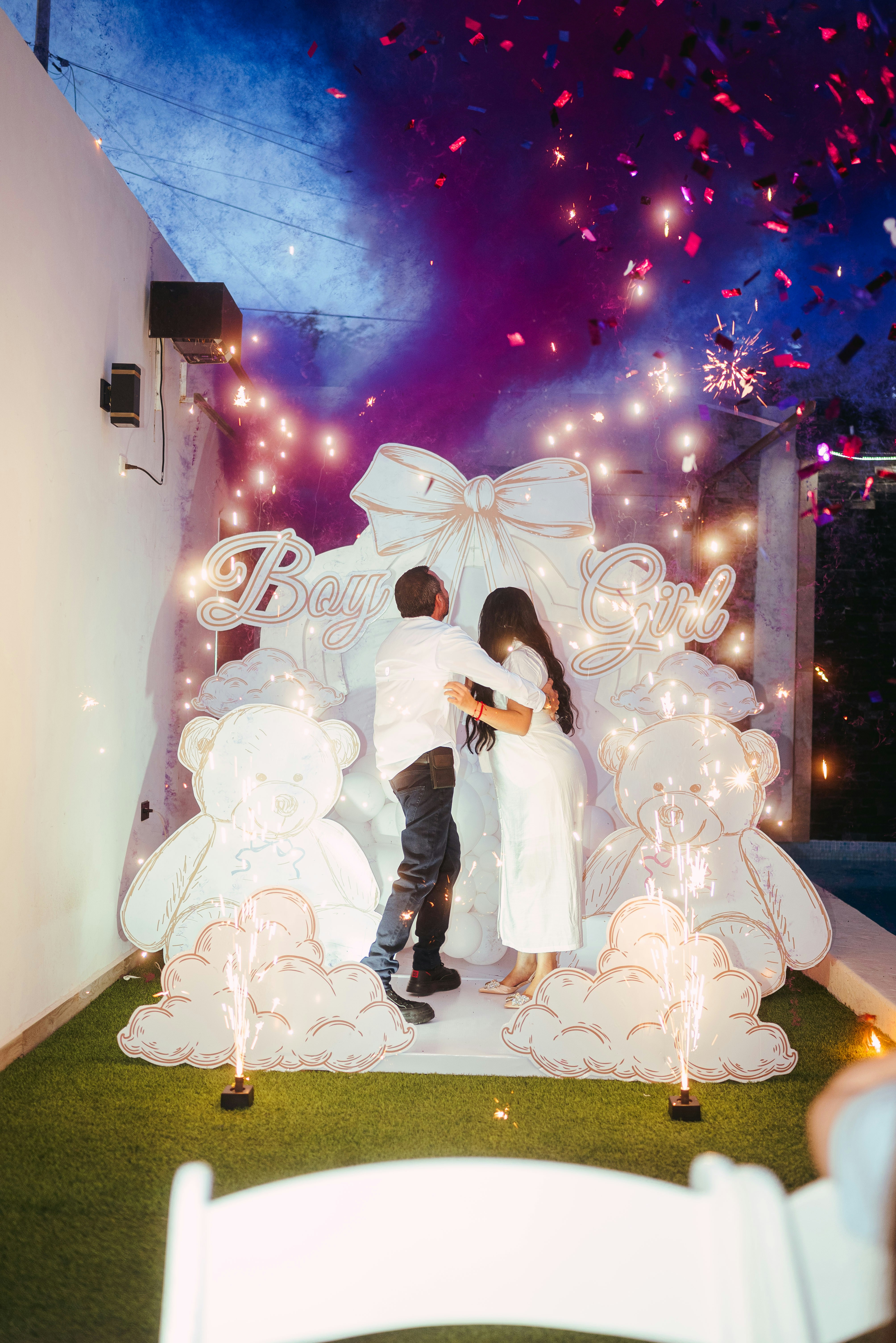 Couple embraces during a gender reveal with confetti and smoke.