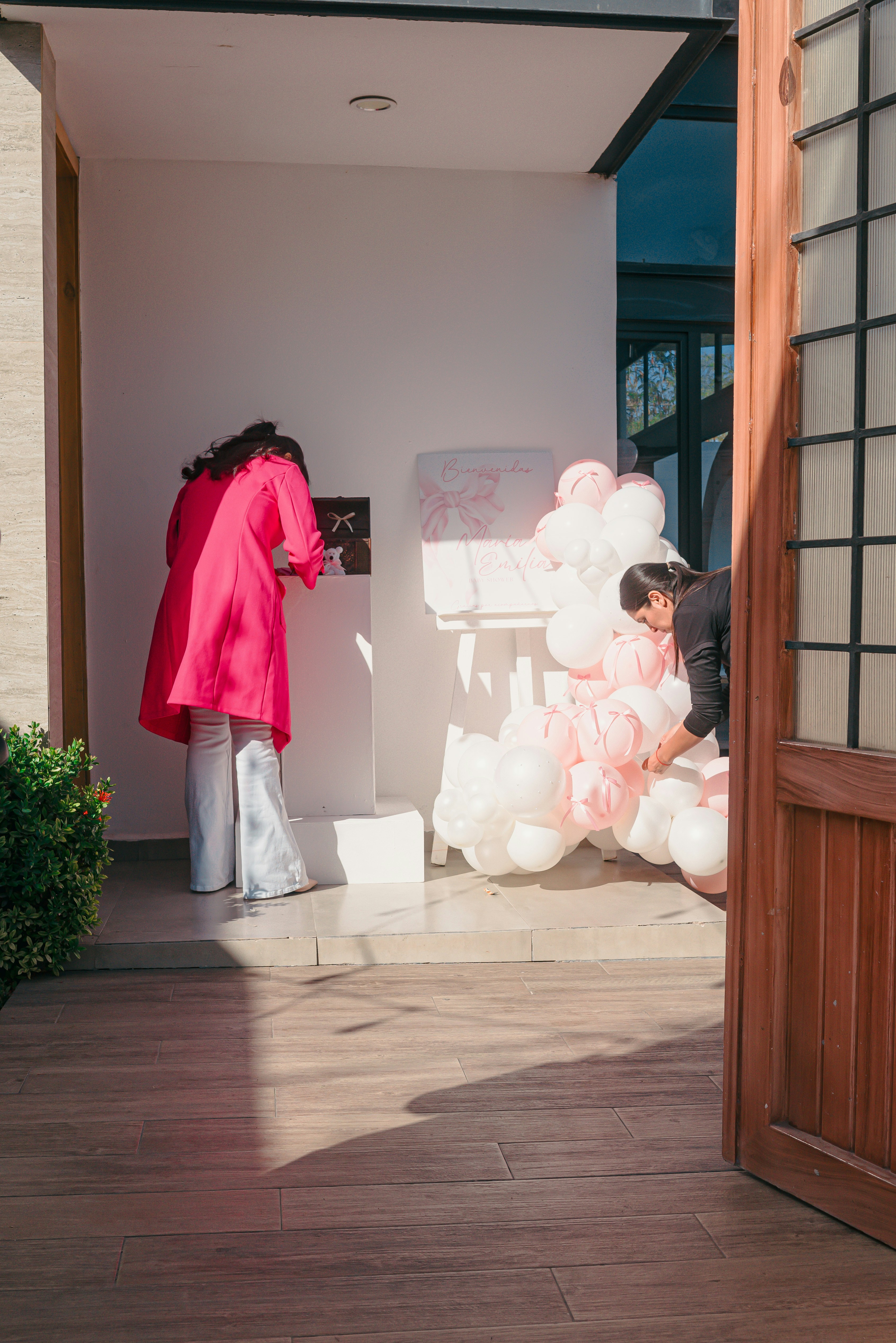 Two women decorating with pink and white balloons.