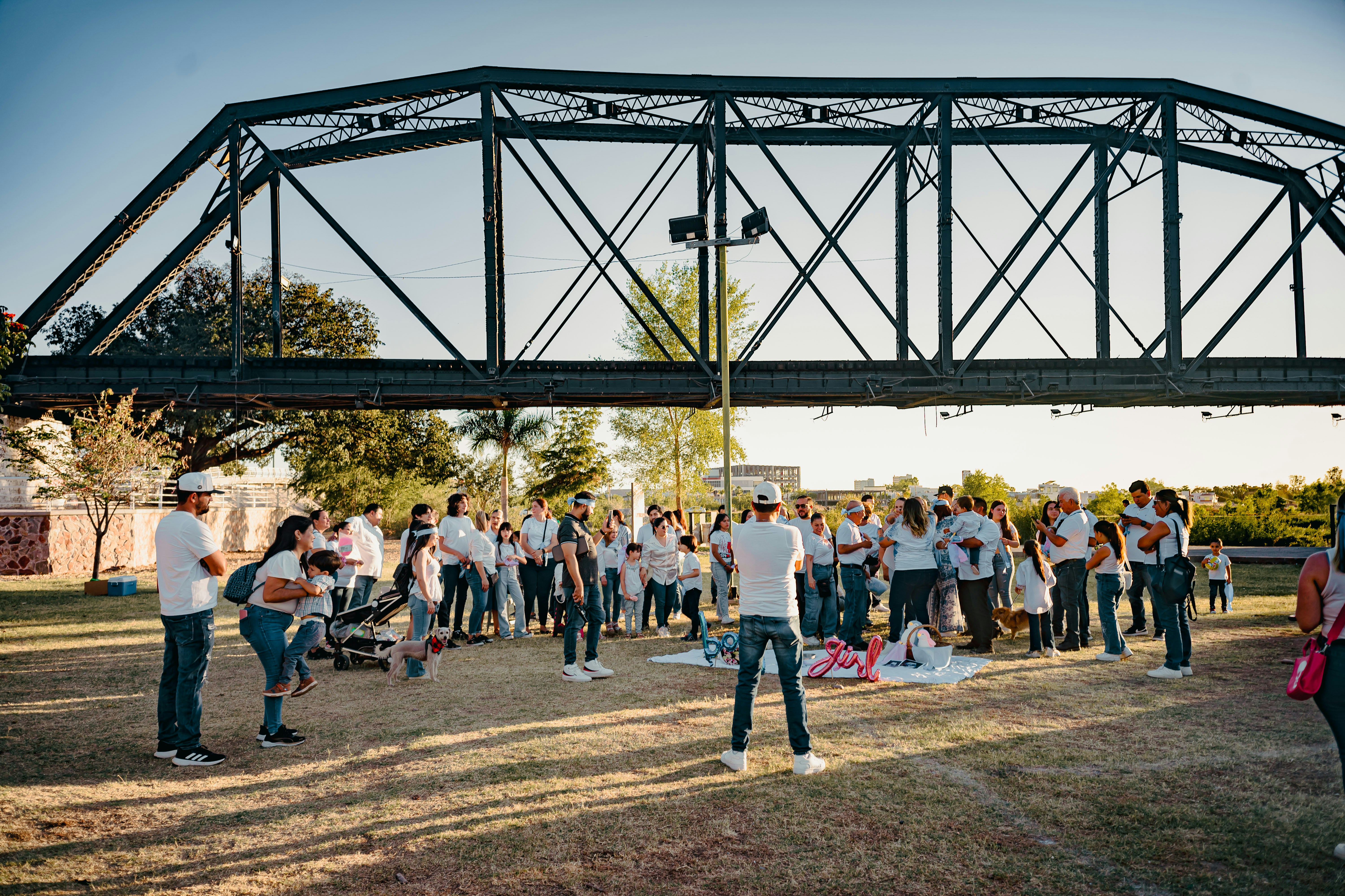 A group of people gathered under a bridge at sunset.