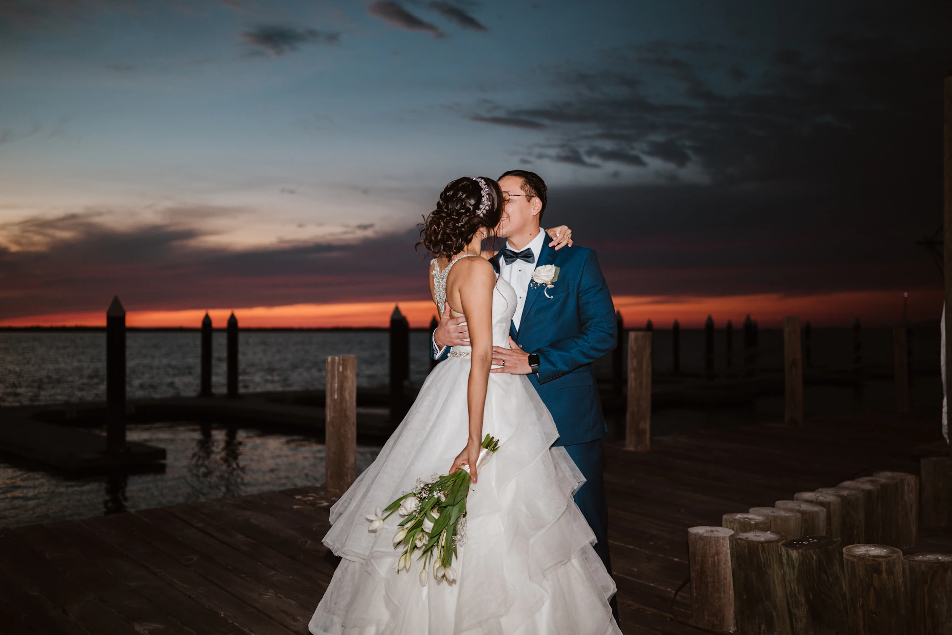 Bride and groom sharing a kiss by the water at sunset