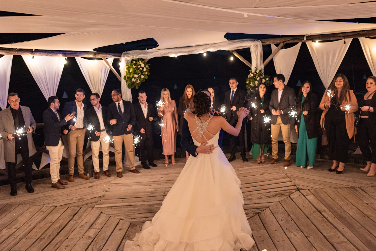 Newlyweds dancing while friends and family surround them with sparklers