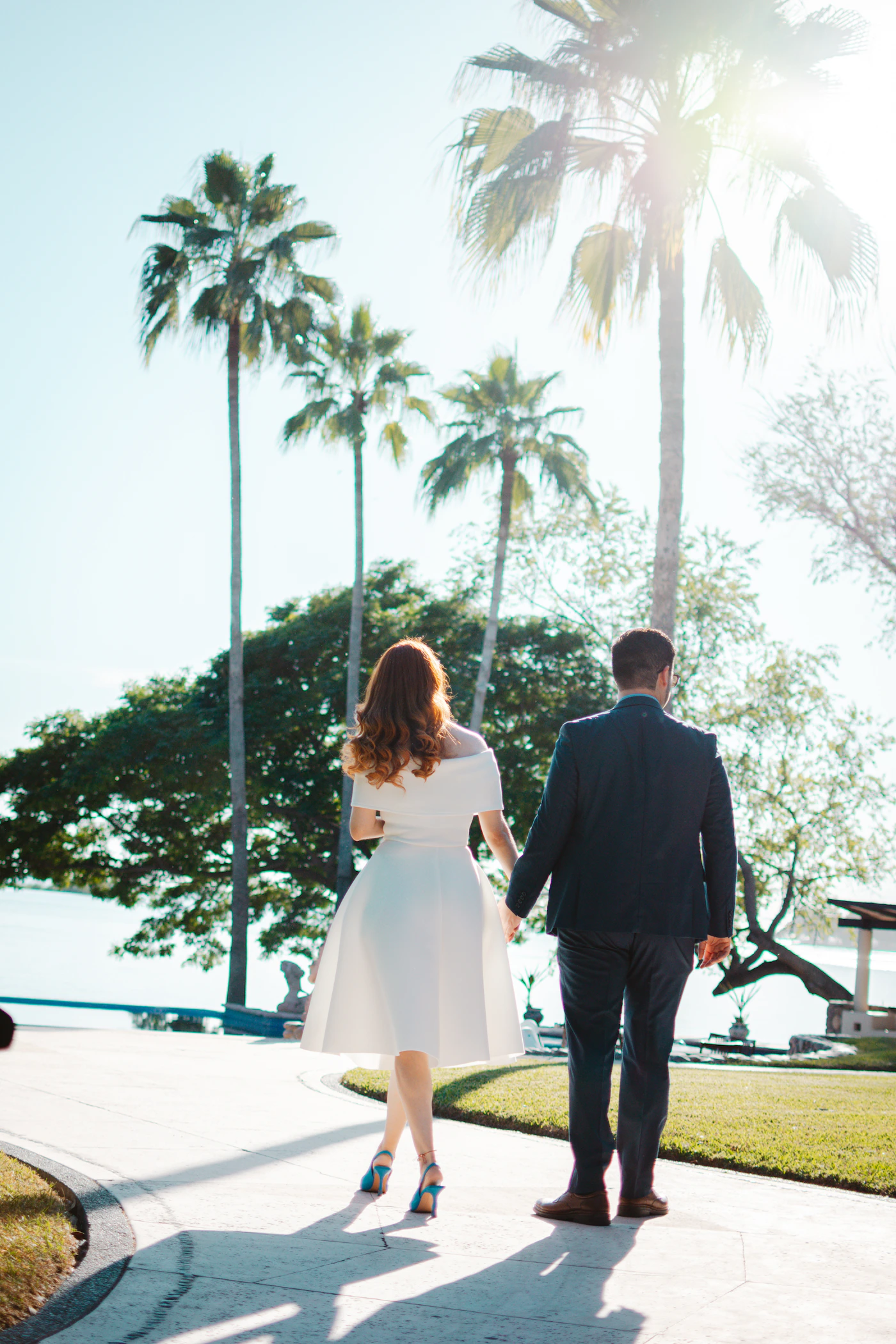 Couple in wedding attire walking together toward tall tropical palms