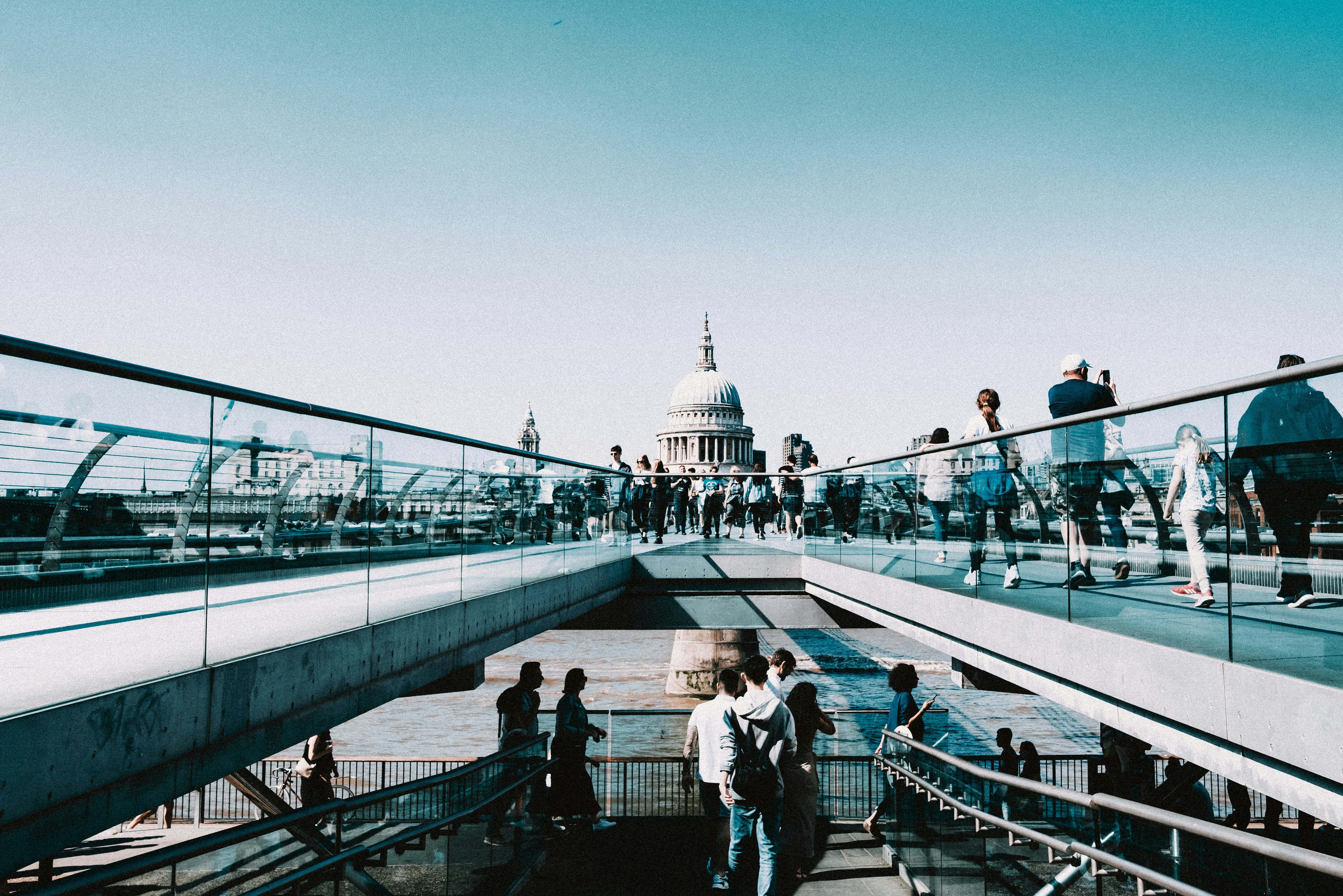 People walking on a modern bridge with dome building.