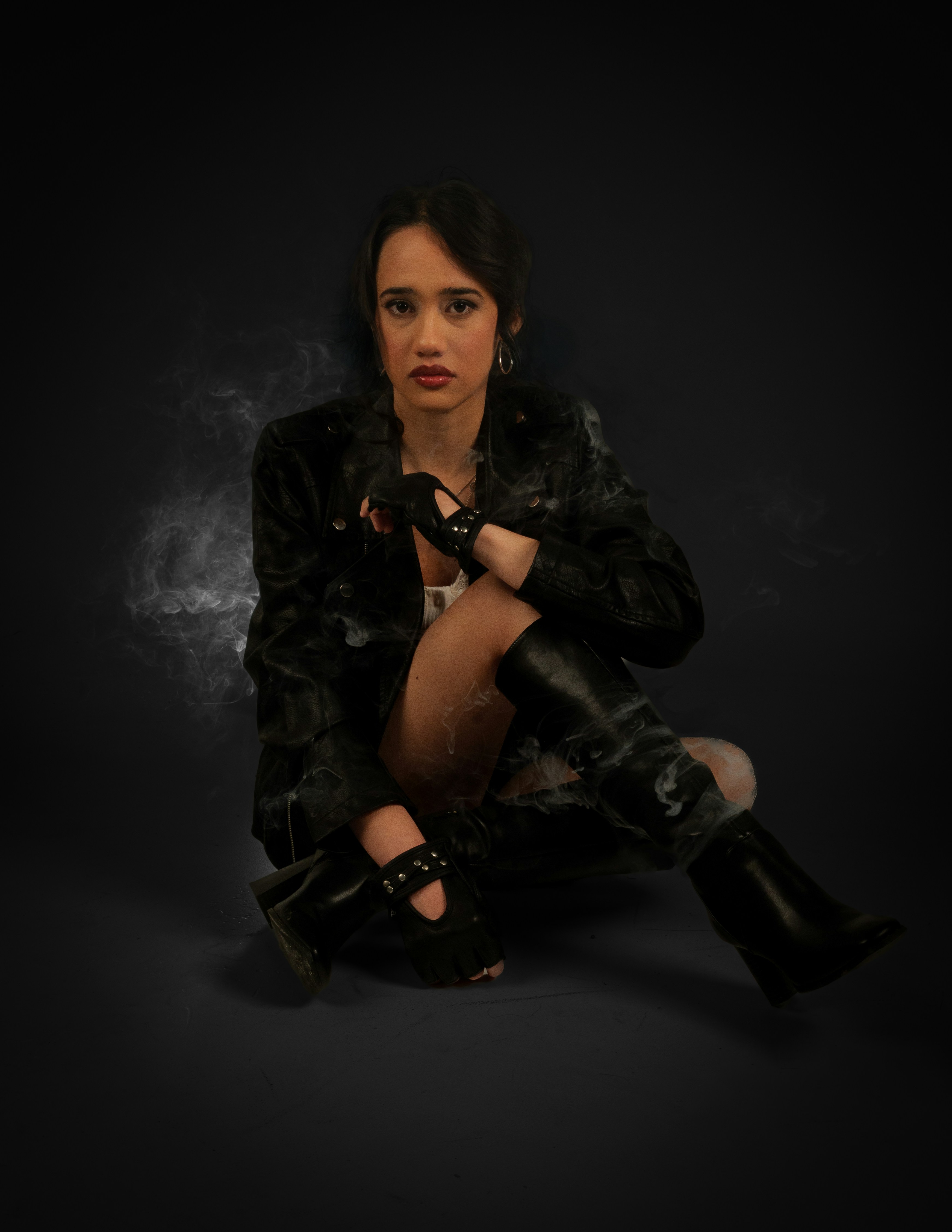 Woman in leather jacket and boots sitting on floor.