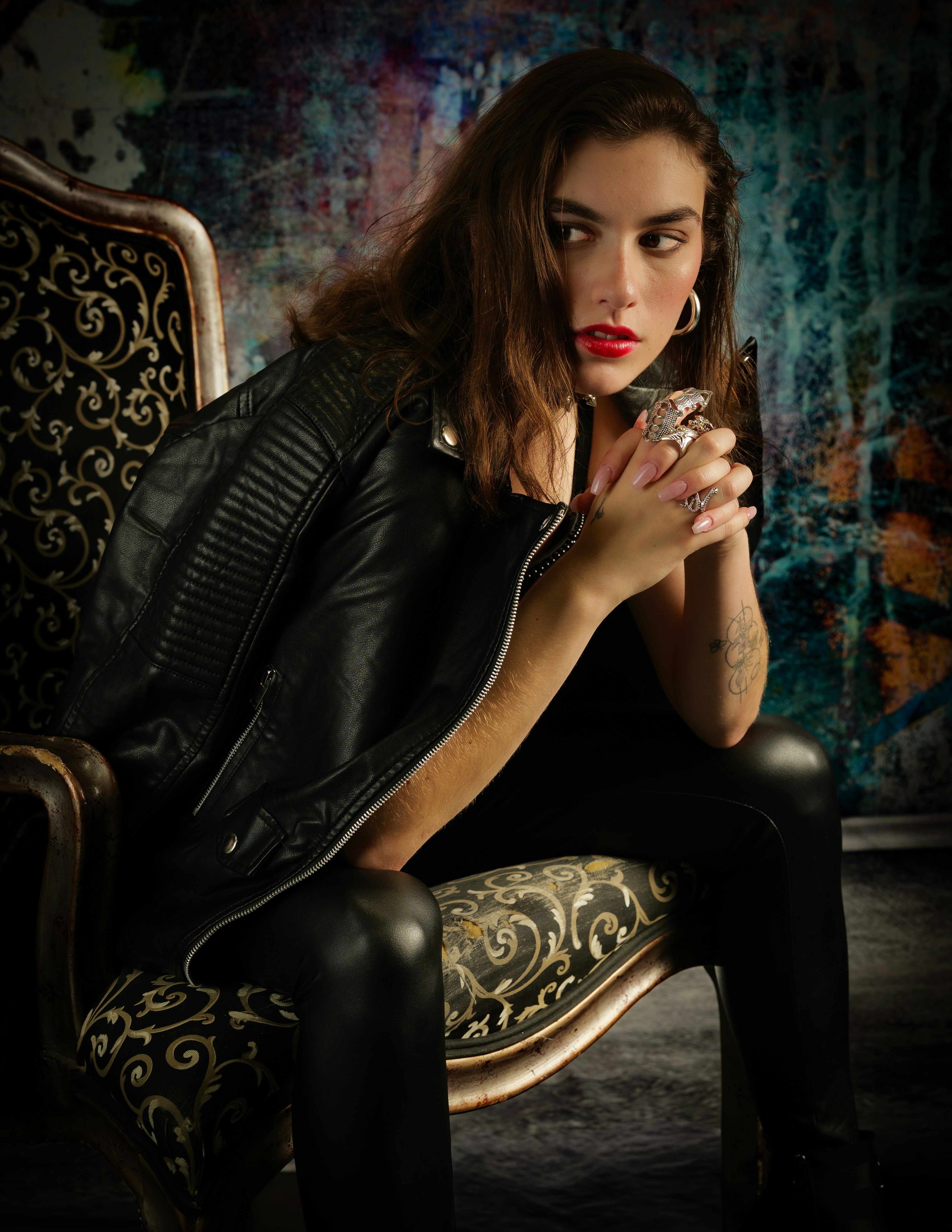 Woman in leather jacket sits in ornate chair