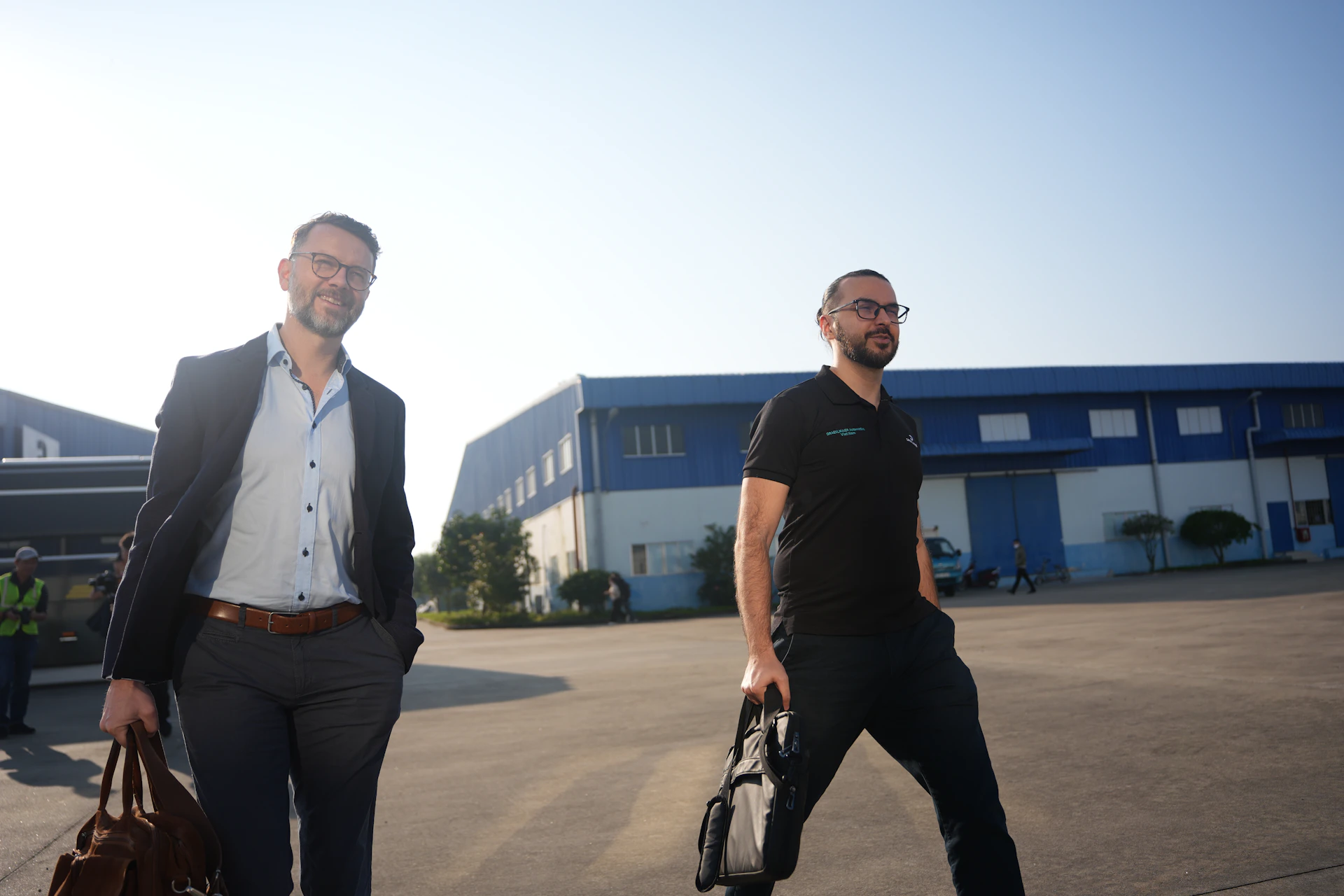 Two men walking with briefcases outside industrial buildings