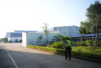 A person in a vest stands near industrial buildings.