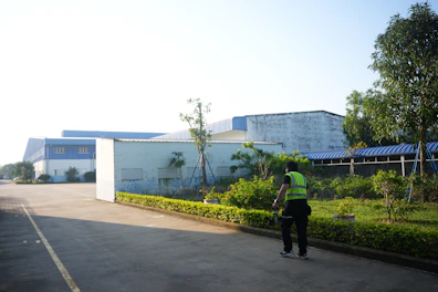 A person in a vest stands near industrial buildings.