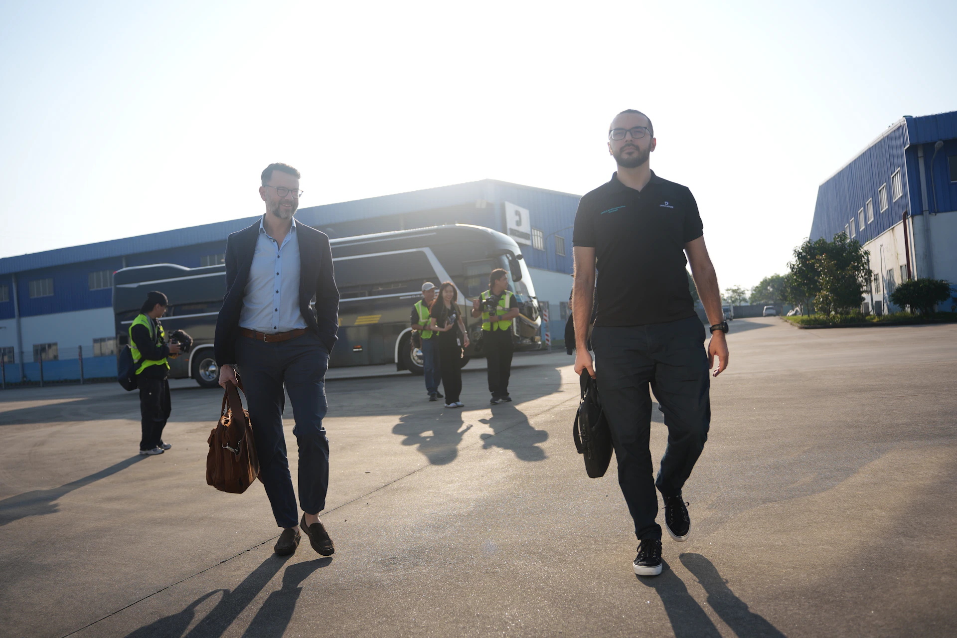 Two men walking with a bus and building behind them