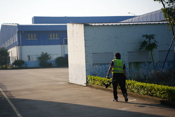Person in reflective vest walks near industrial buildings.
