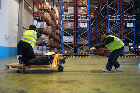Two workers moving pallet with hand truck in warehouse
