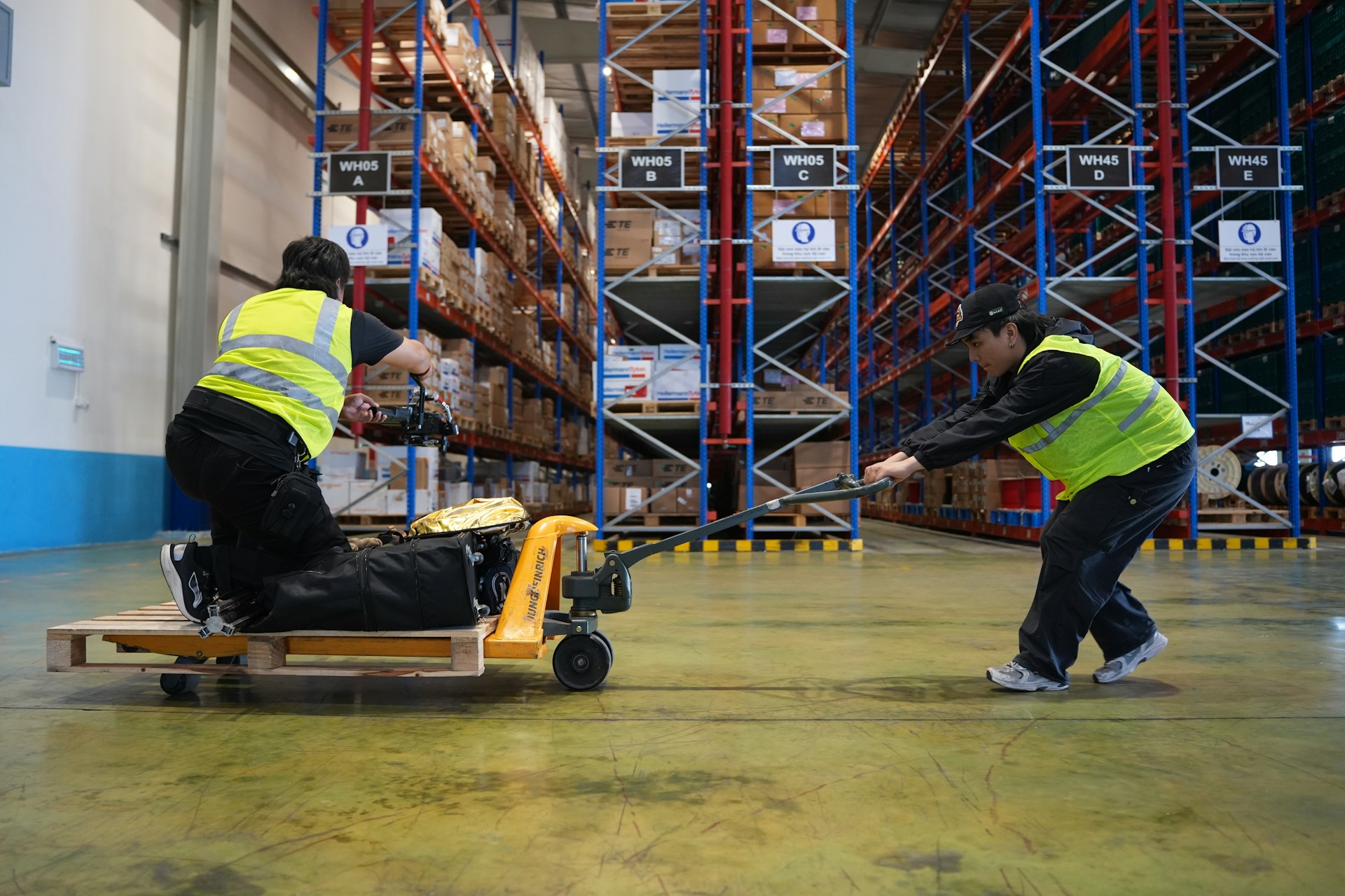 Two workers moving pallet with hand truck in warehouse