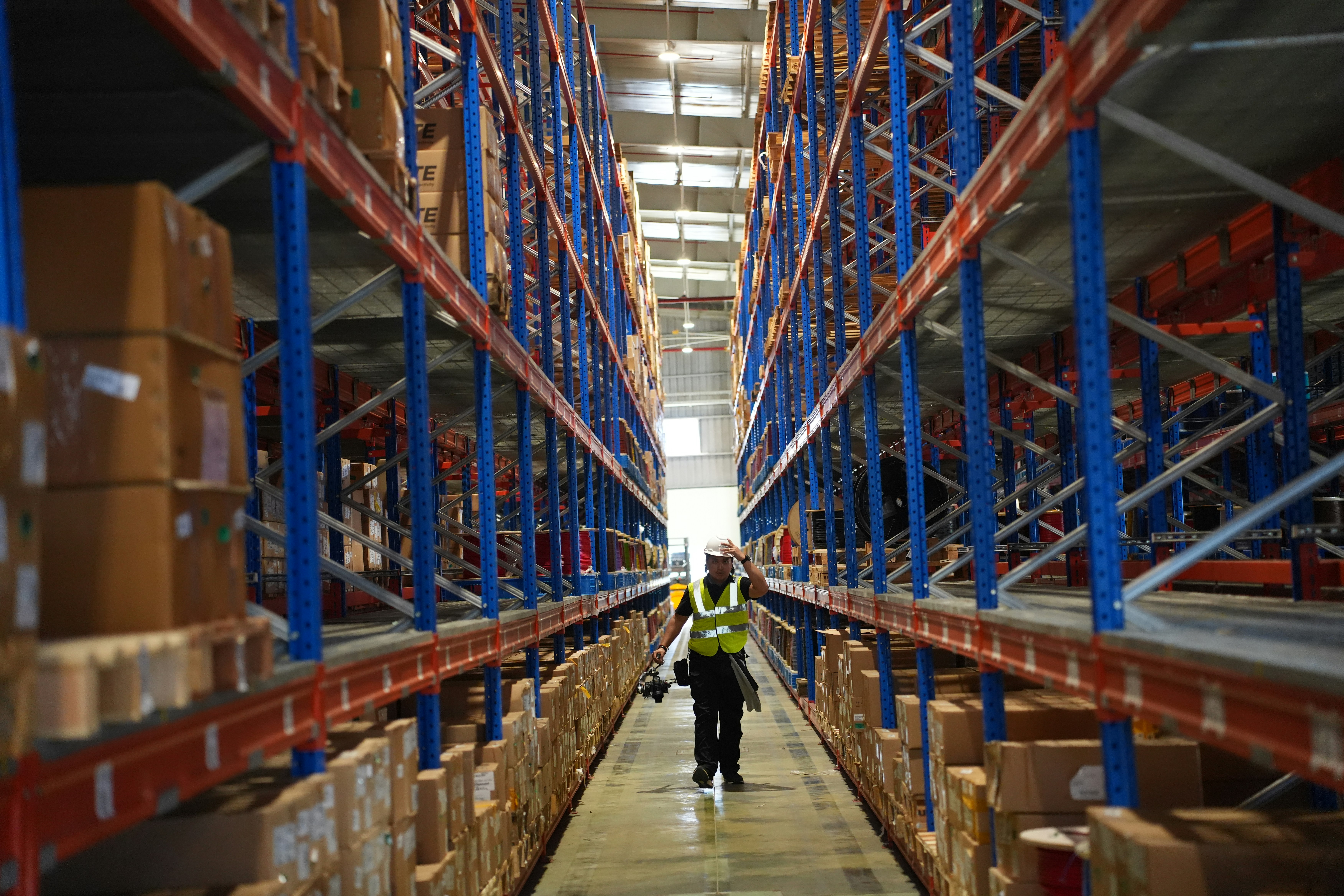 Worker walks through a large warehouse with tall shelves.