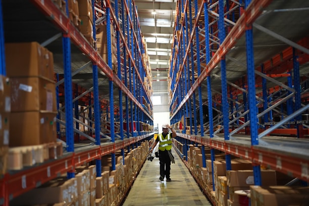 Worker walks through a large warehouse with tall shelves.