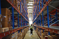 Worker walks through a large warehouse with tall shelves.