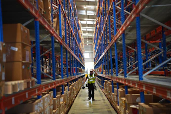 Worker walks through a large warehouse with tall shelves.