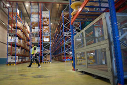 Man walks through a brightly lit warehouse with tall shelves.