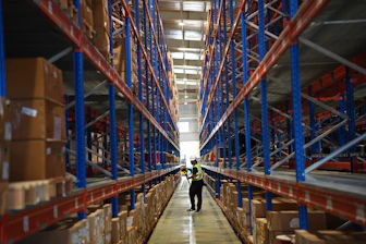 Man walking down aisle in a large warehouse with shelves.