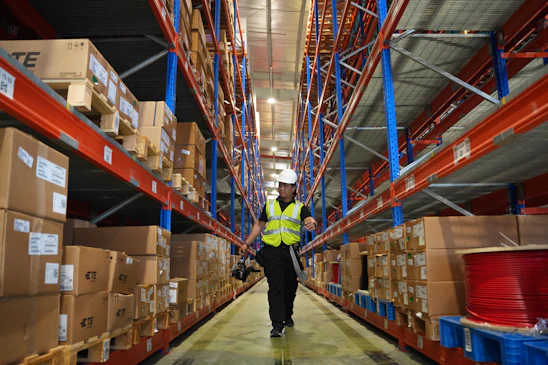 Man in reflective vest walks down warehouse aisle.