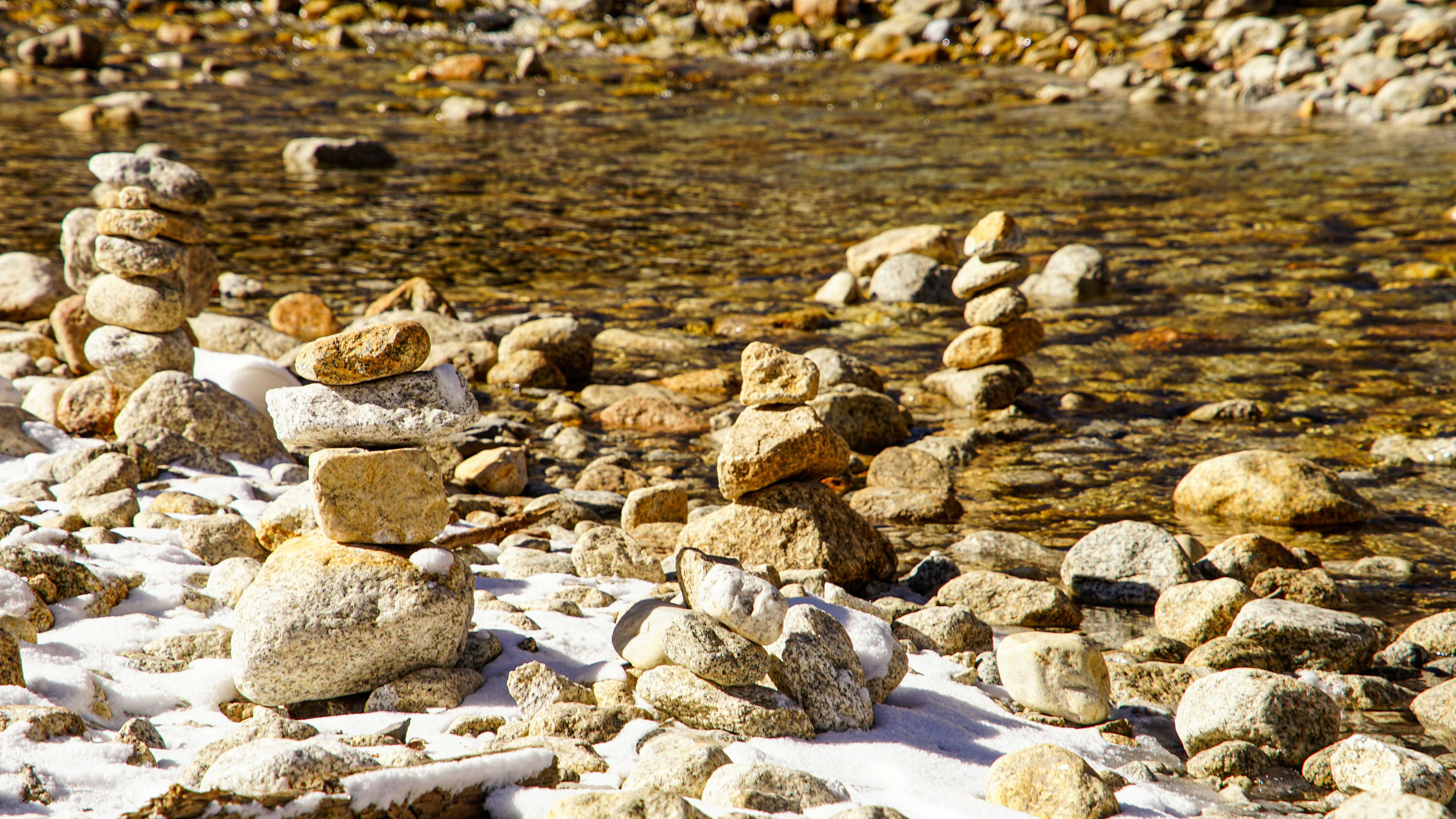 Stacked rocks by a shallow stream with snow.