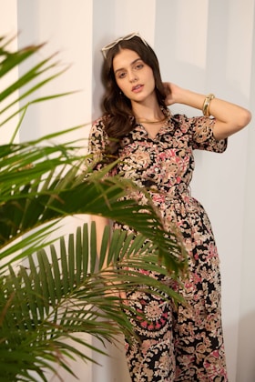 Woman in floral jumpsuit leans against wall