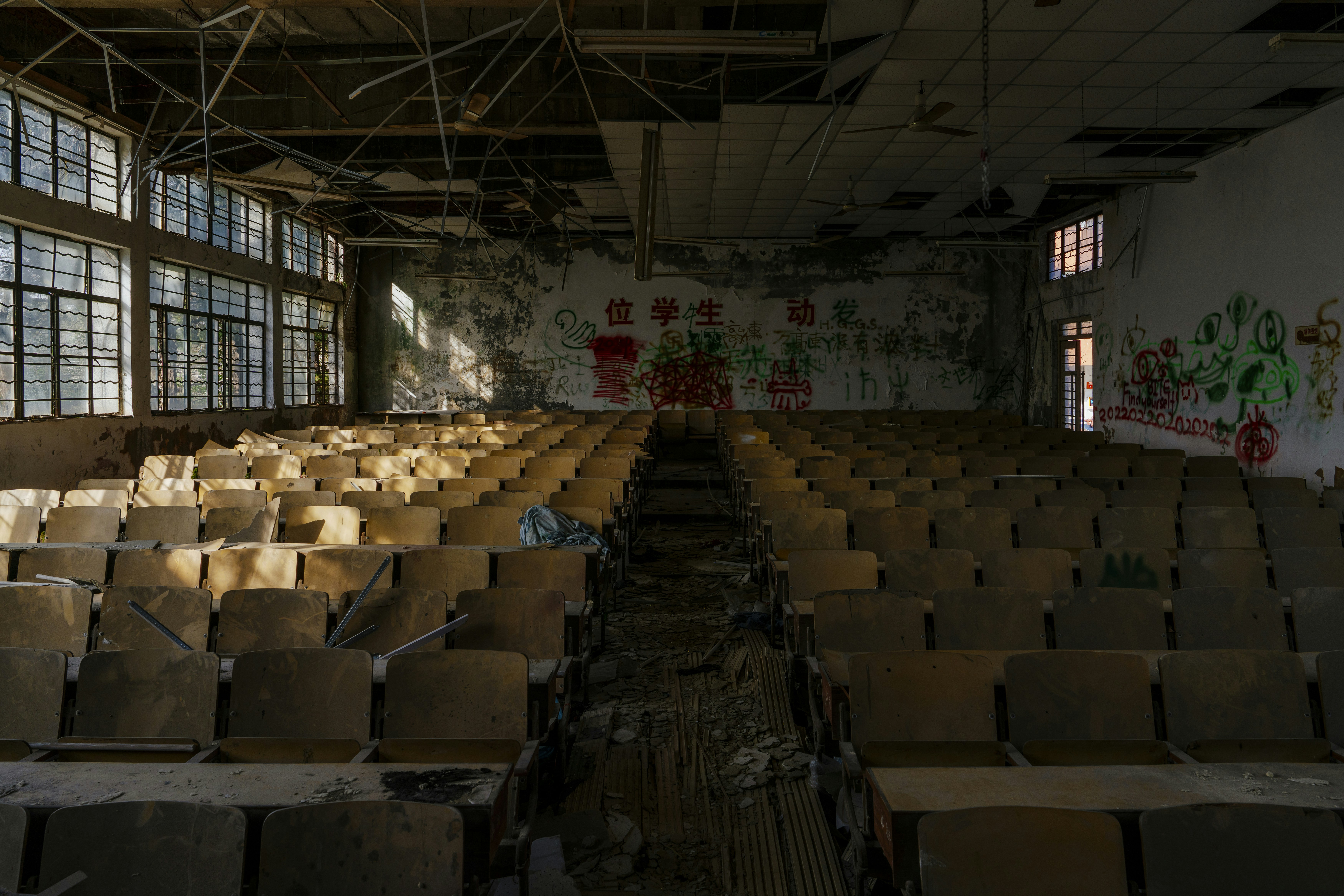 Abandoned auditorium with rows of empty seats and graffiti.
