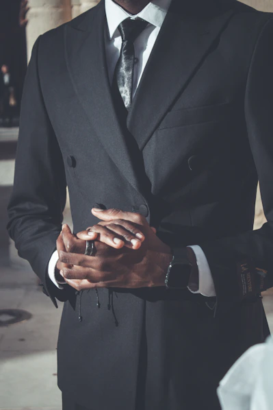 Man in a black double-breasted suit with hands clasped